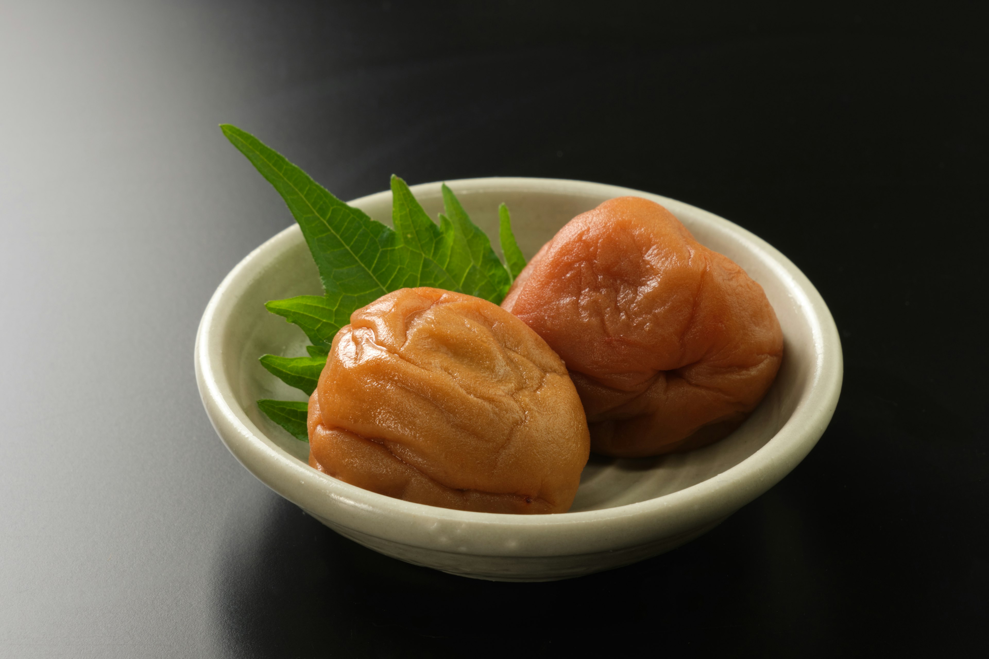 Pickled umeboshi plums with green leaves in a white bowl