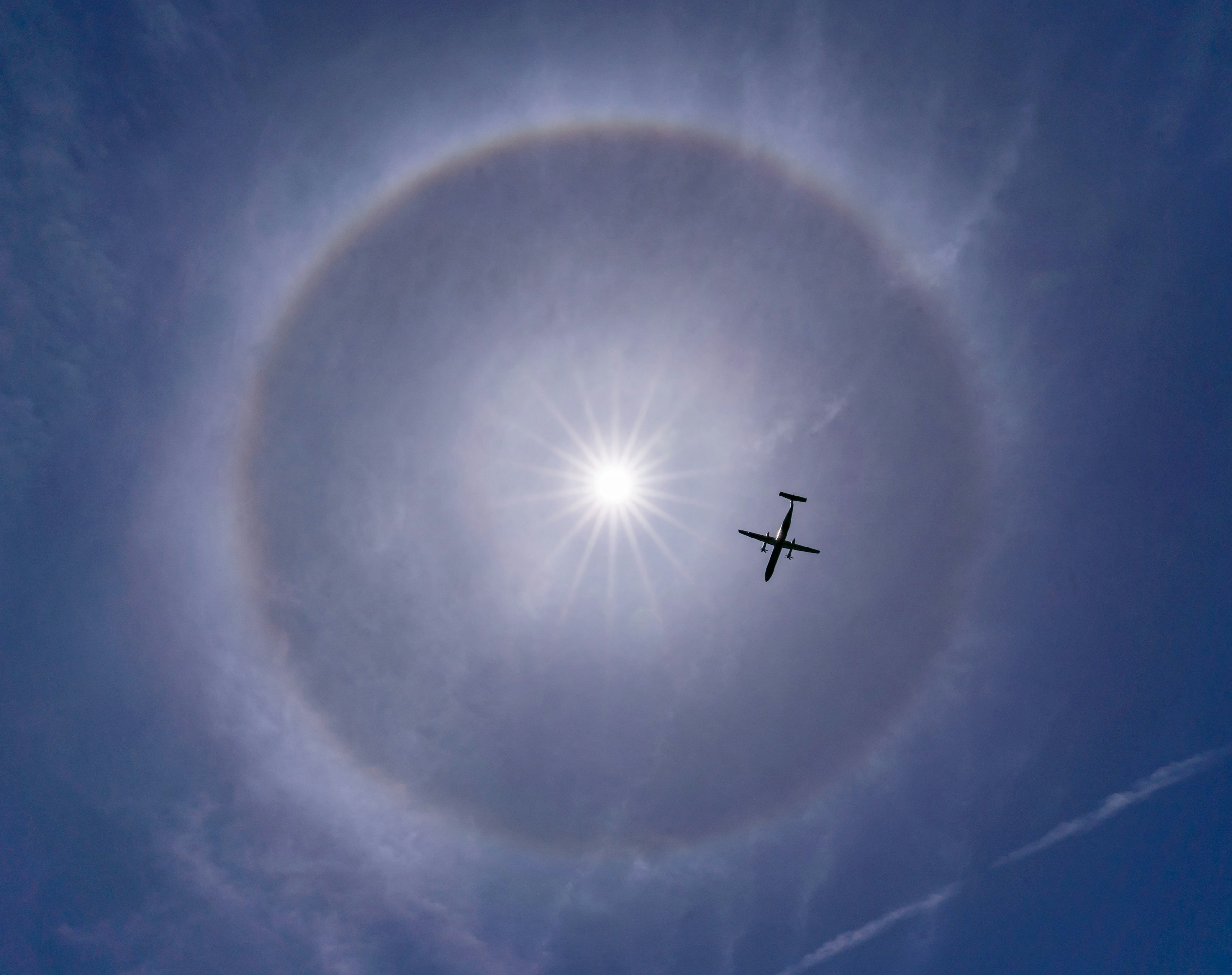 Pesawat terbang melawan halo matahari yang cerah di langit biru