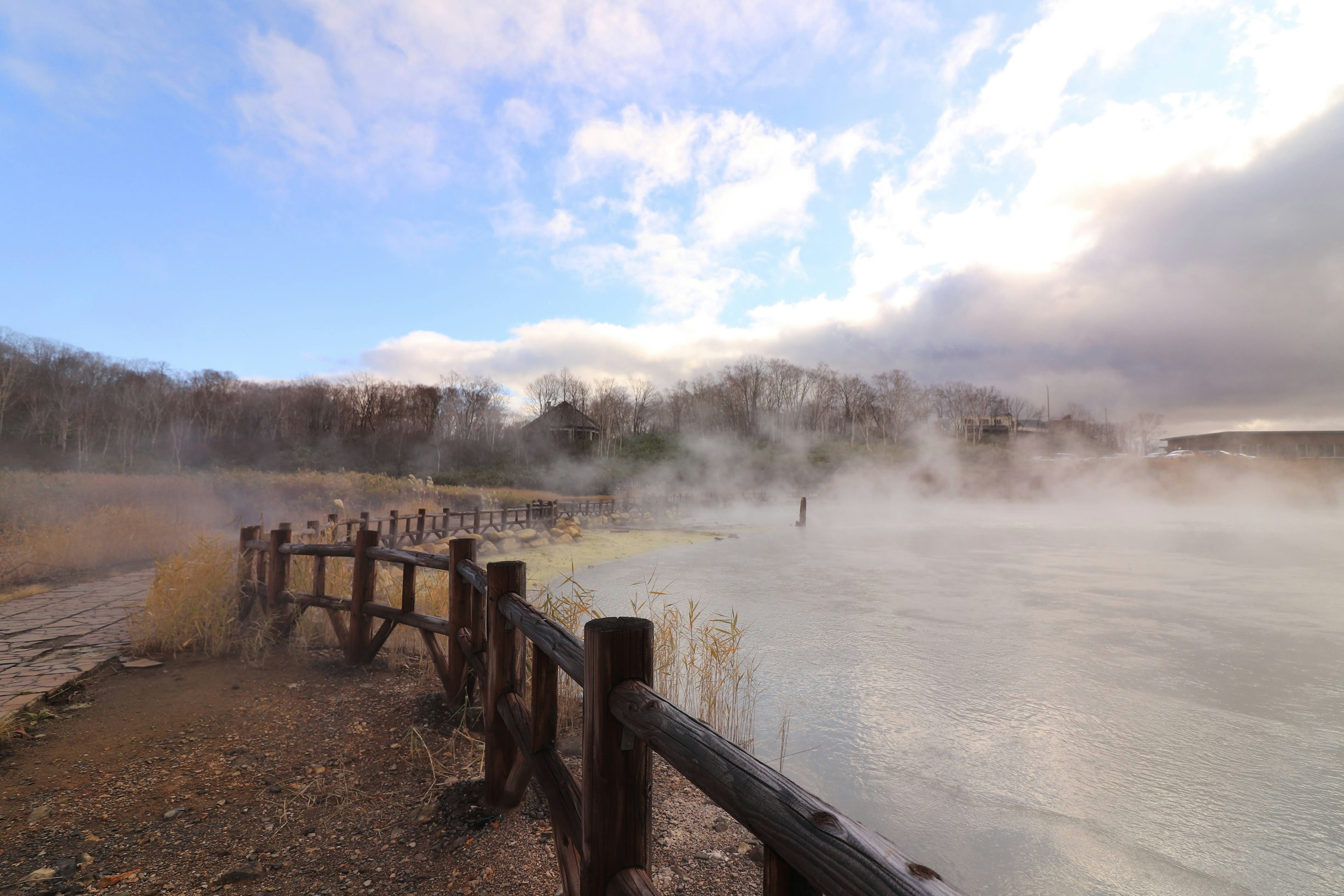 Wooden fence along a hot spring with rising mist over the water