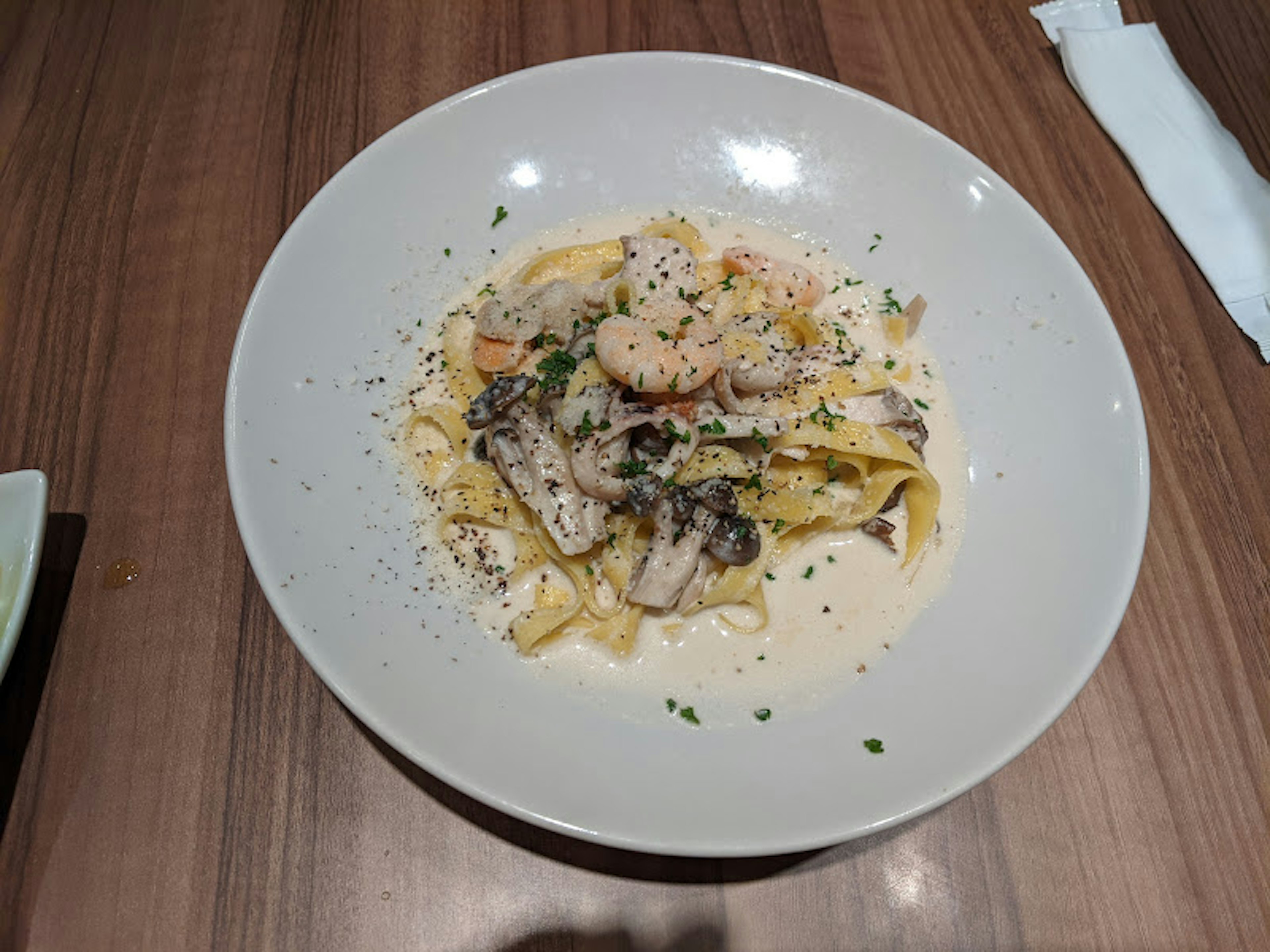 Pâtes crémeuses garnies de fruits de mer et d'herbes servies dans un bol blanc