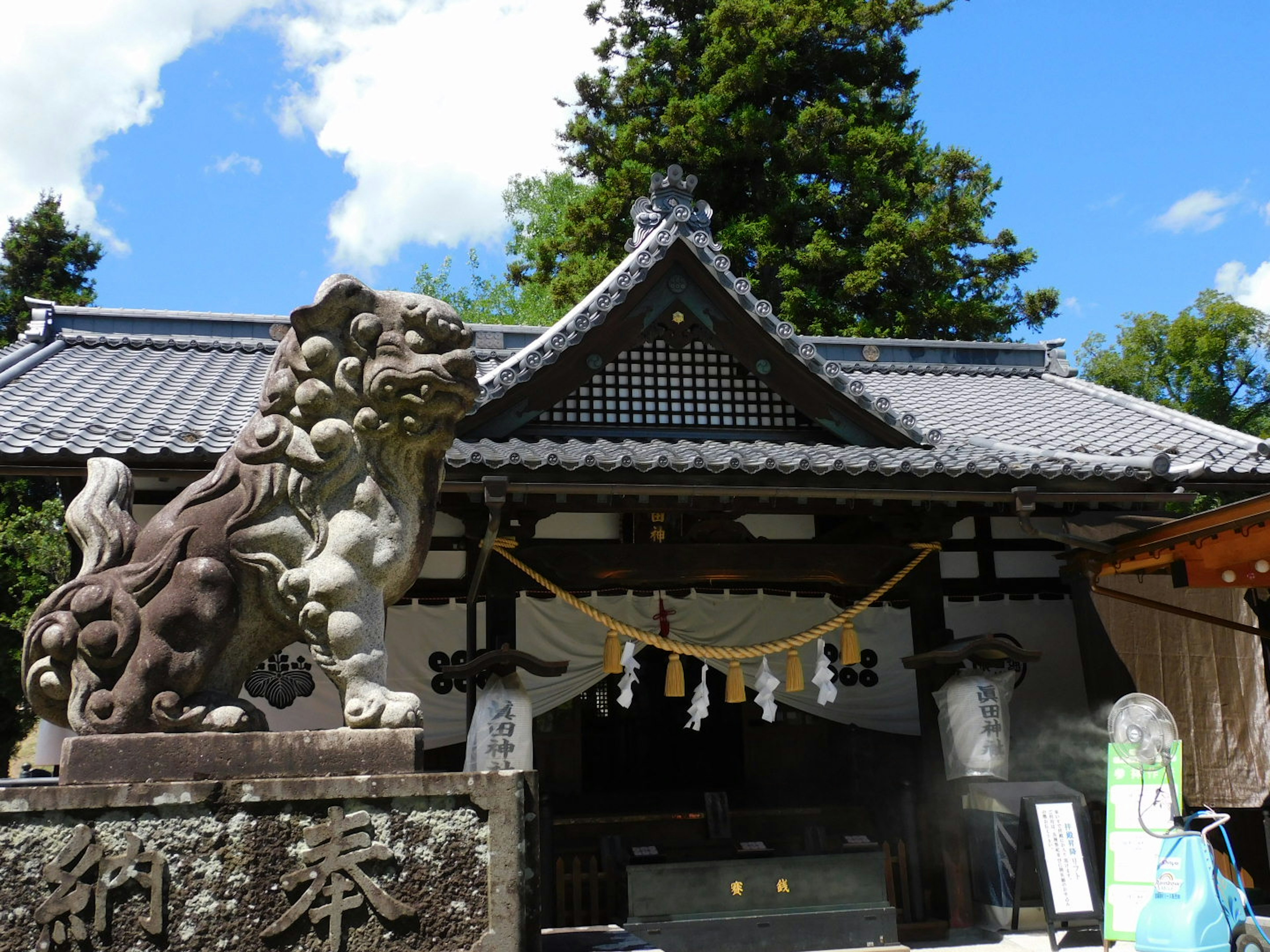 Entrée d'un temple avec une statue de lion gardien et un toit traditionnel sous un ciel bleu