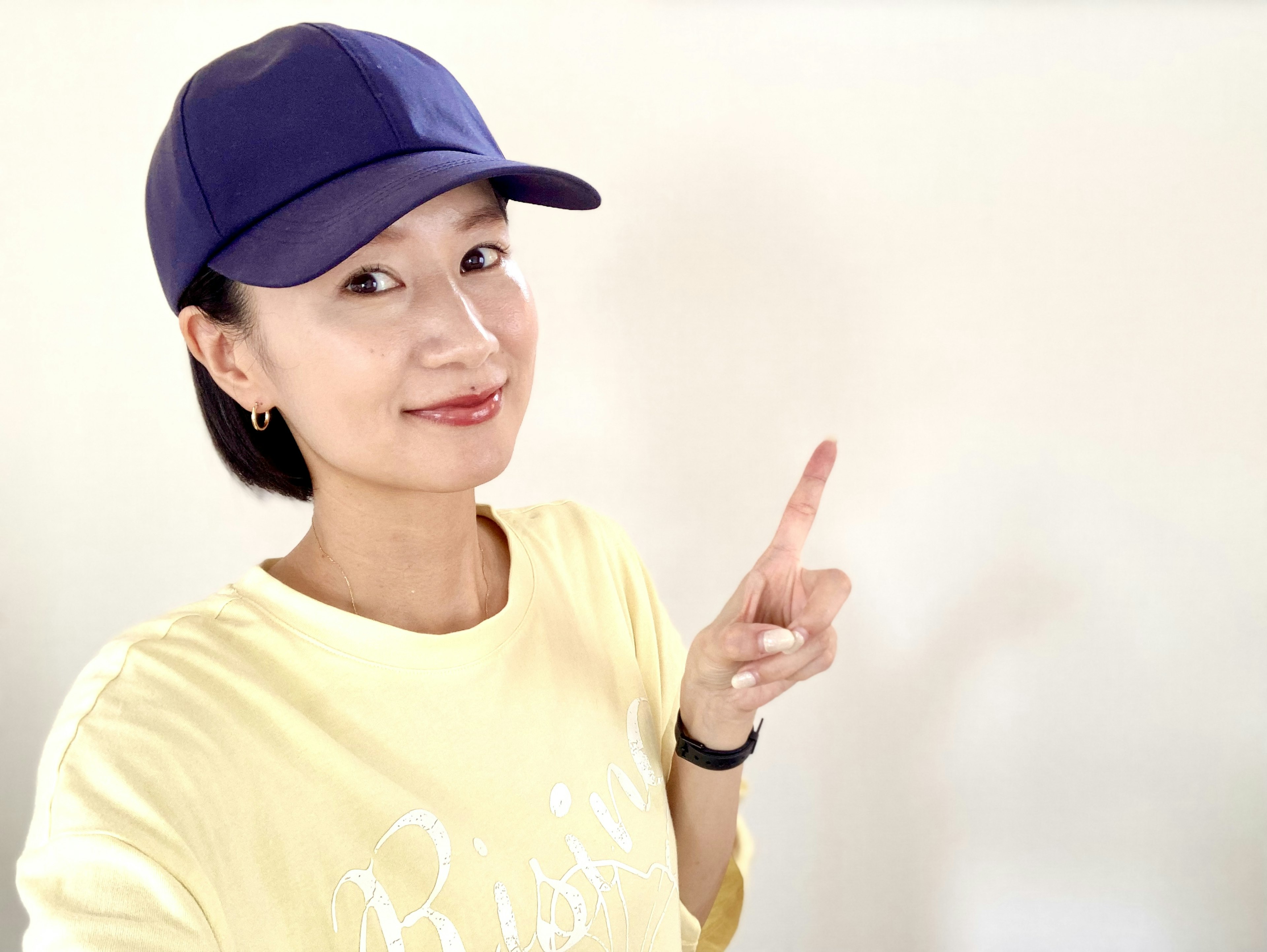 A woman wearing a purple cap is smiling and pointing upwards