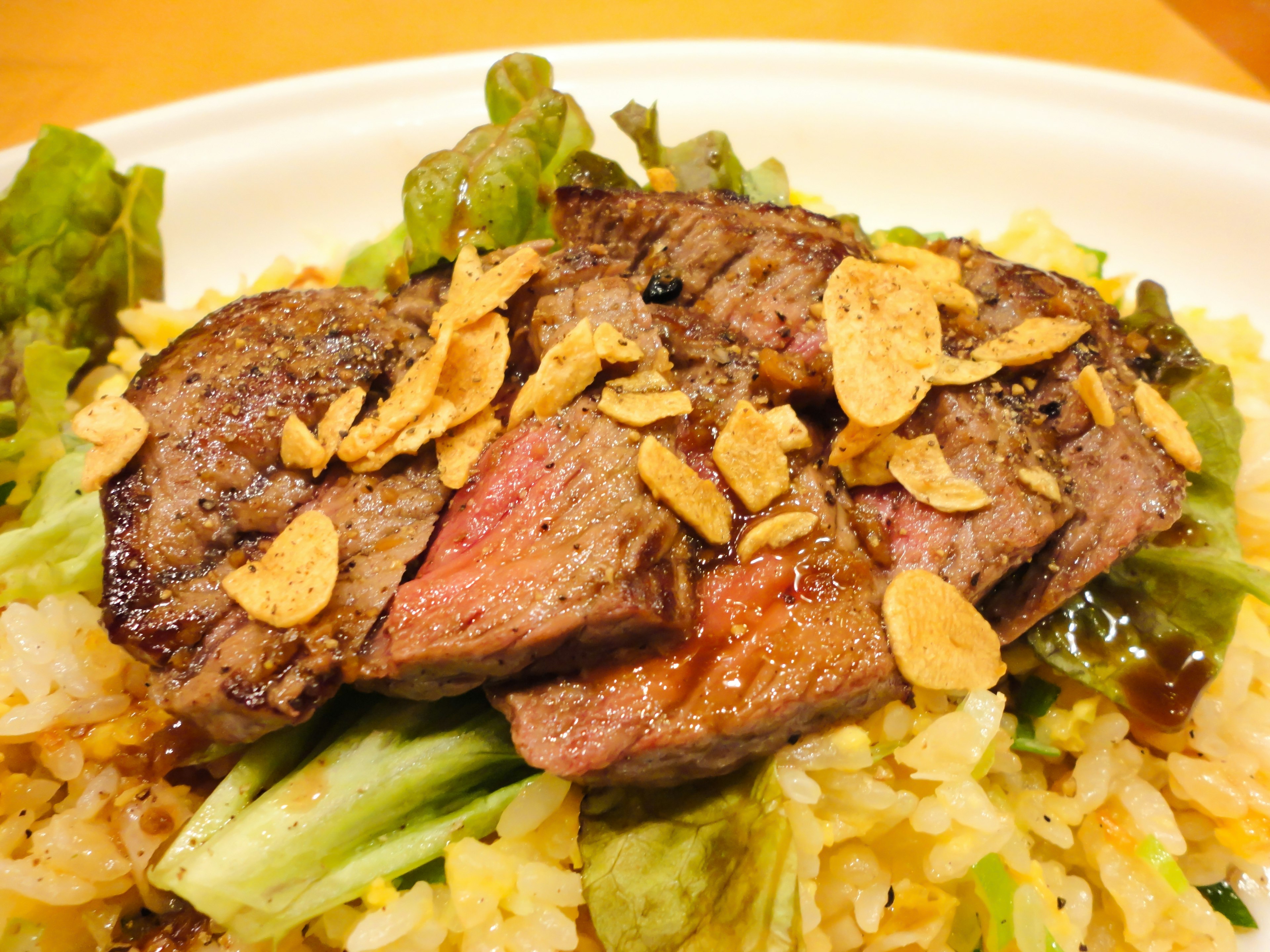 Plate of grilled steak served over rice with garlic chips on top