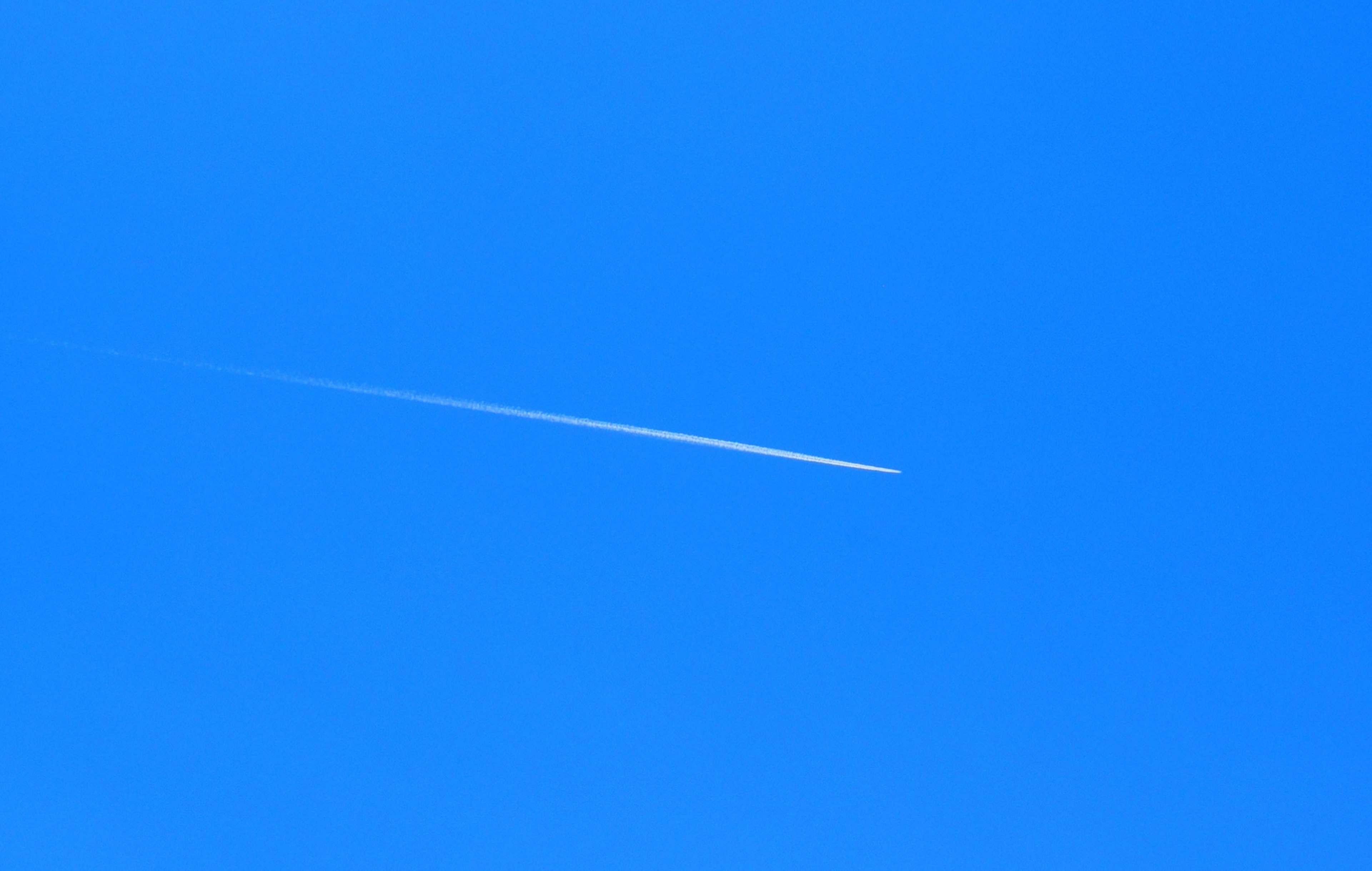 A simple scene of a white contrail in a blue sky