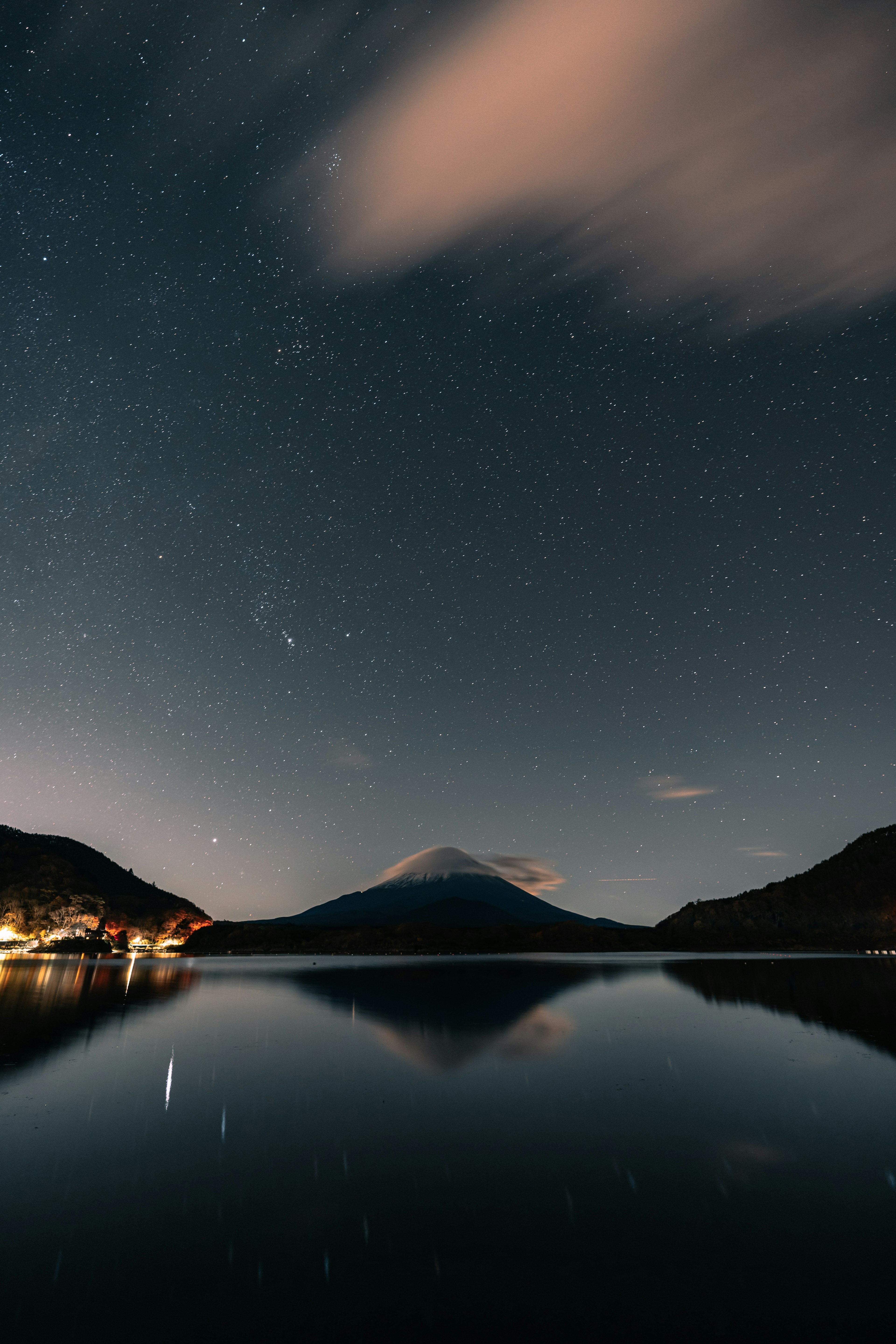 星空と山の夜景が映る静かな湖の風景