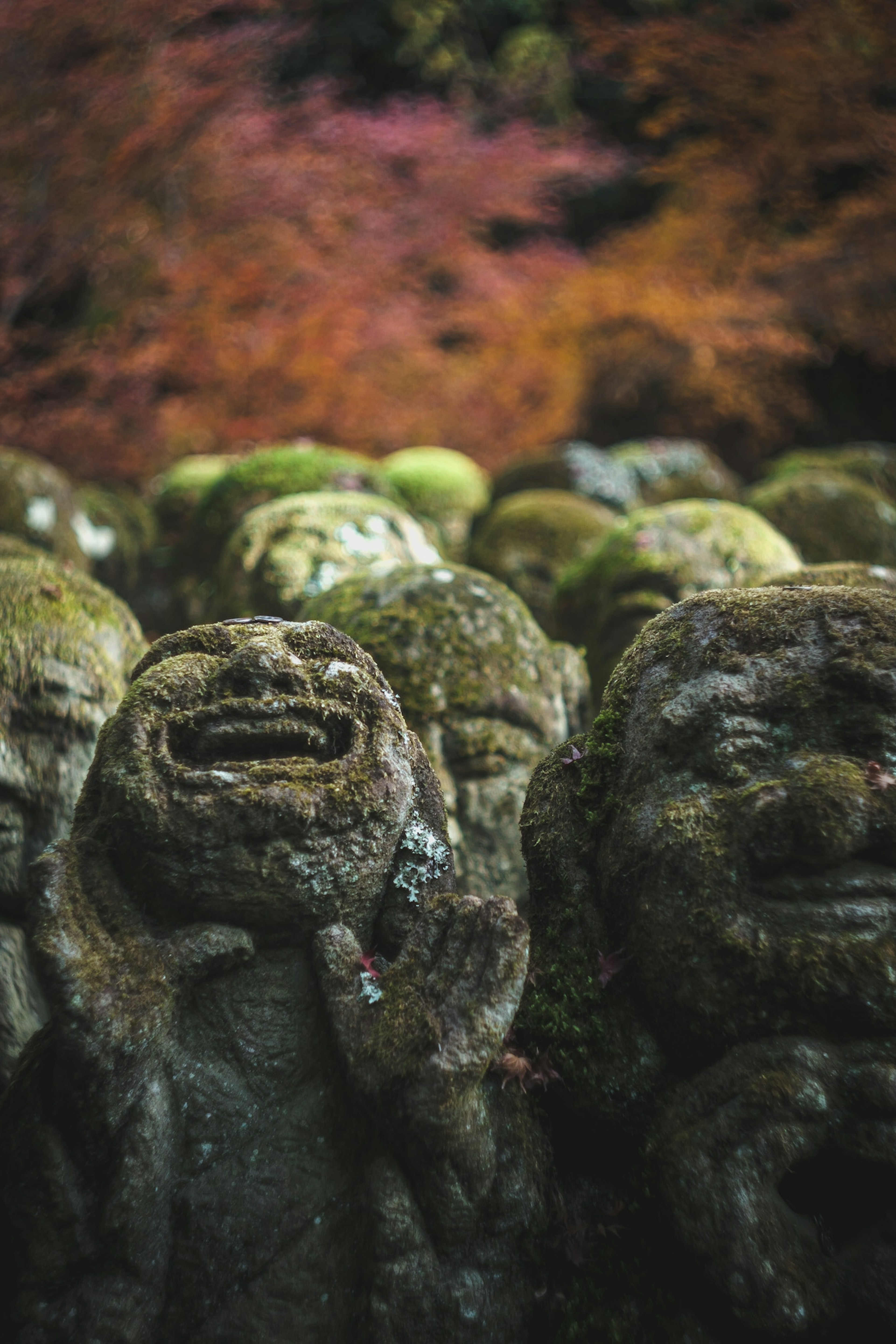 Grupo de figuras de piedra cubiertas de musgo con follaje de otoño al fondo