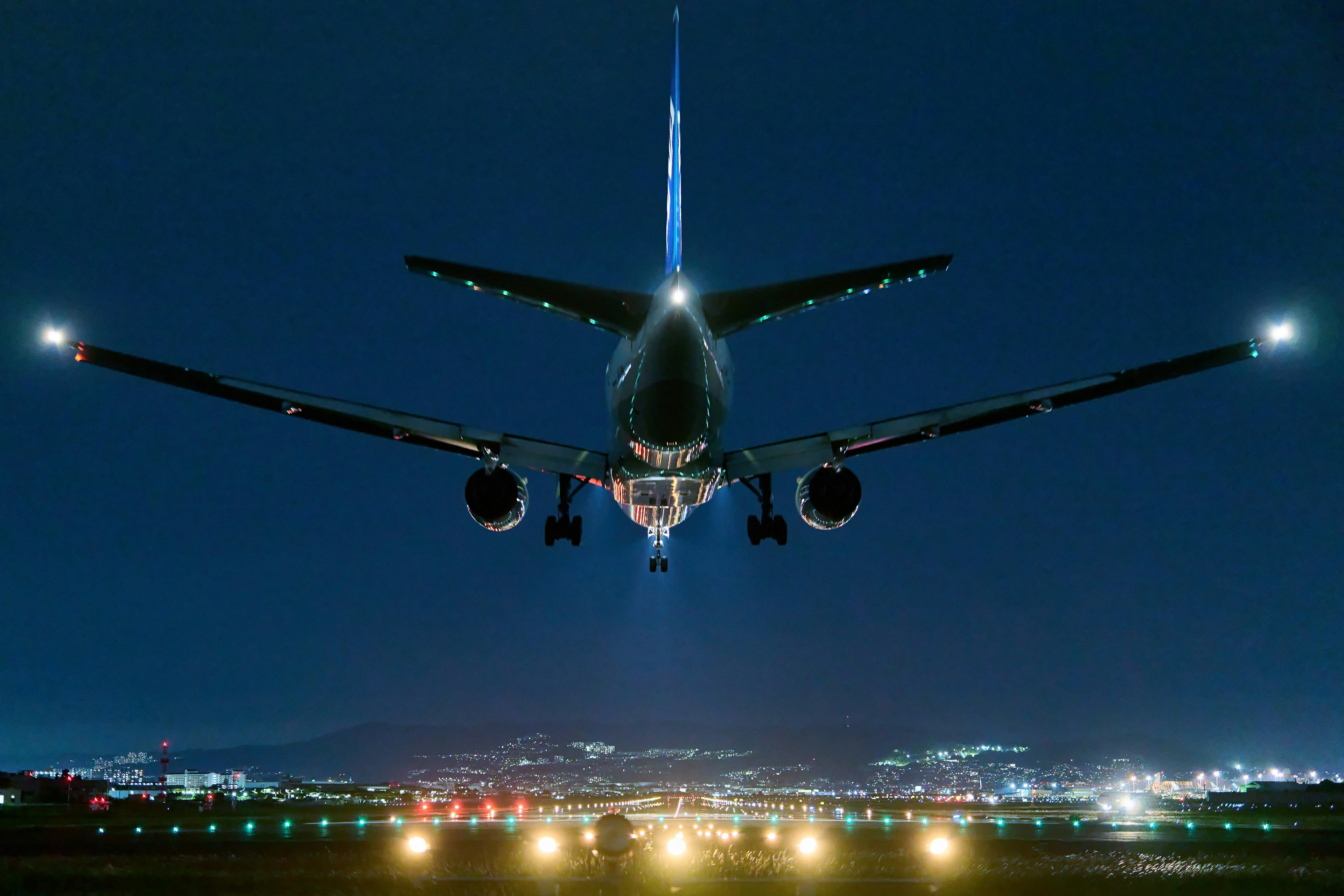 Airplane approaching landing at night illuminated by runway lights and city lights