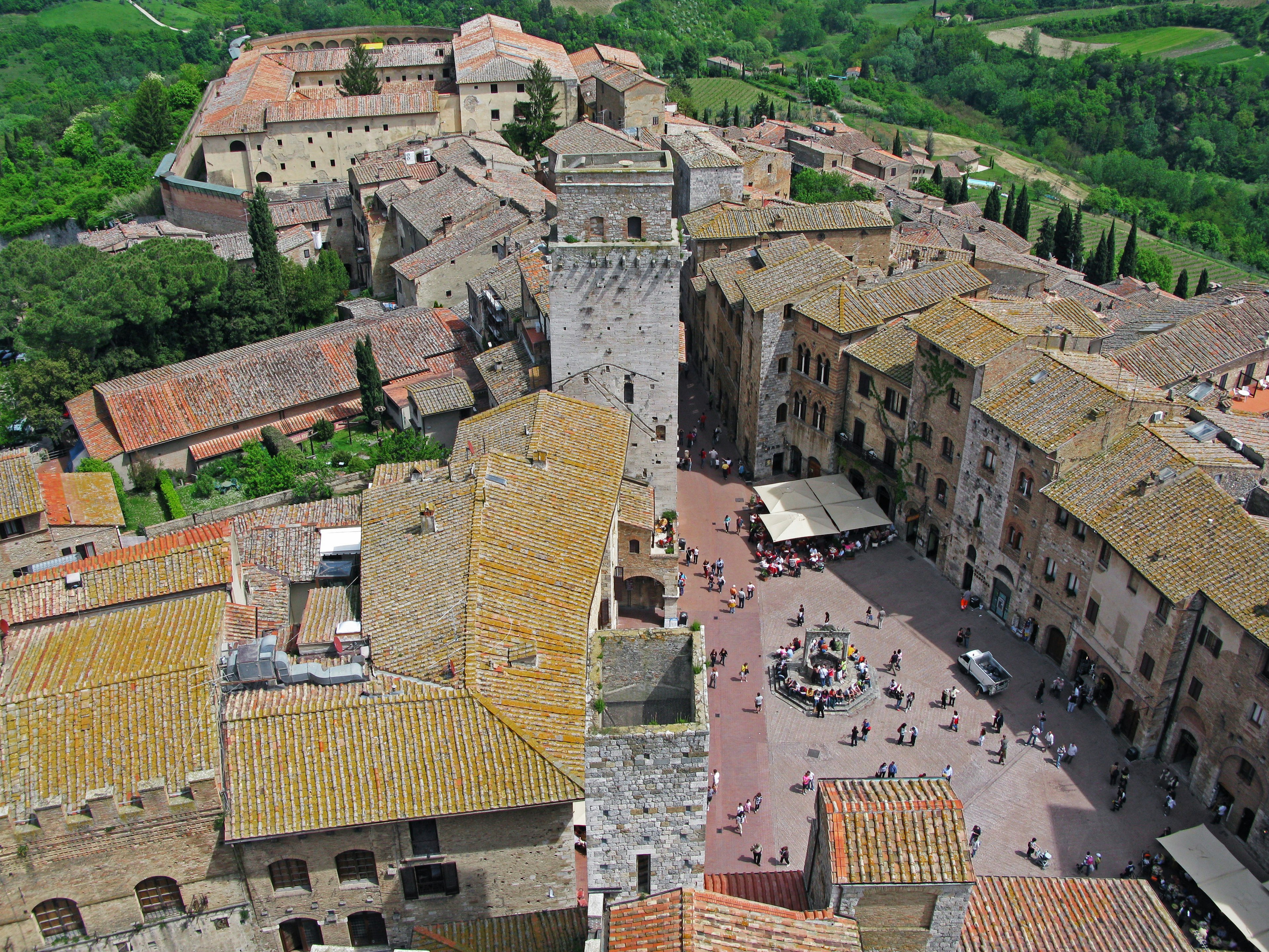 Aerial view of a medieval village in Tuscany surrounded by green hills featuring stone buildings and towers