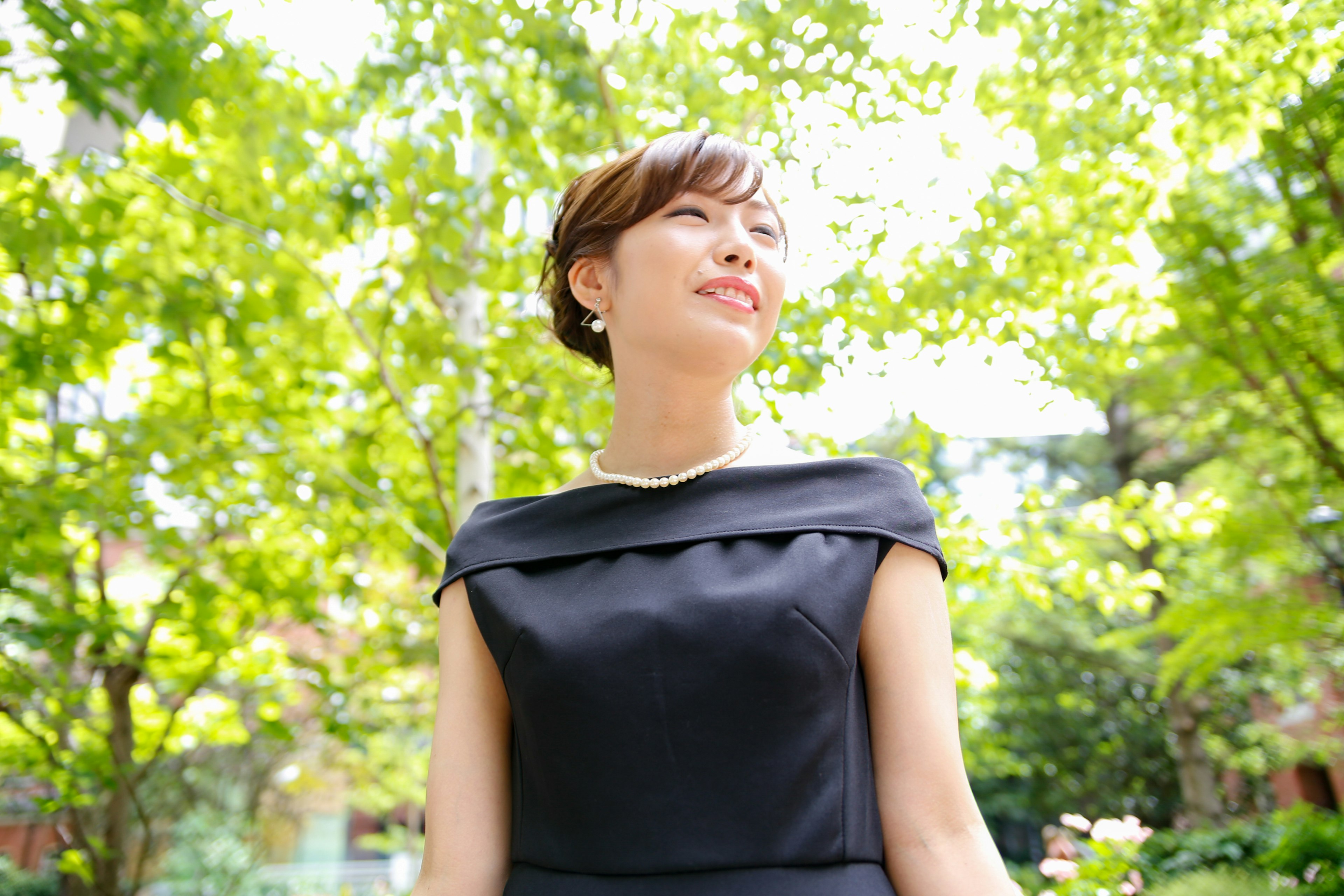 Mujer con vestido negro sonriendo entre árboles verdes