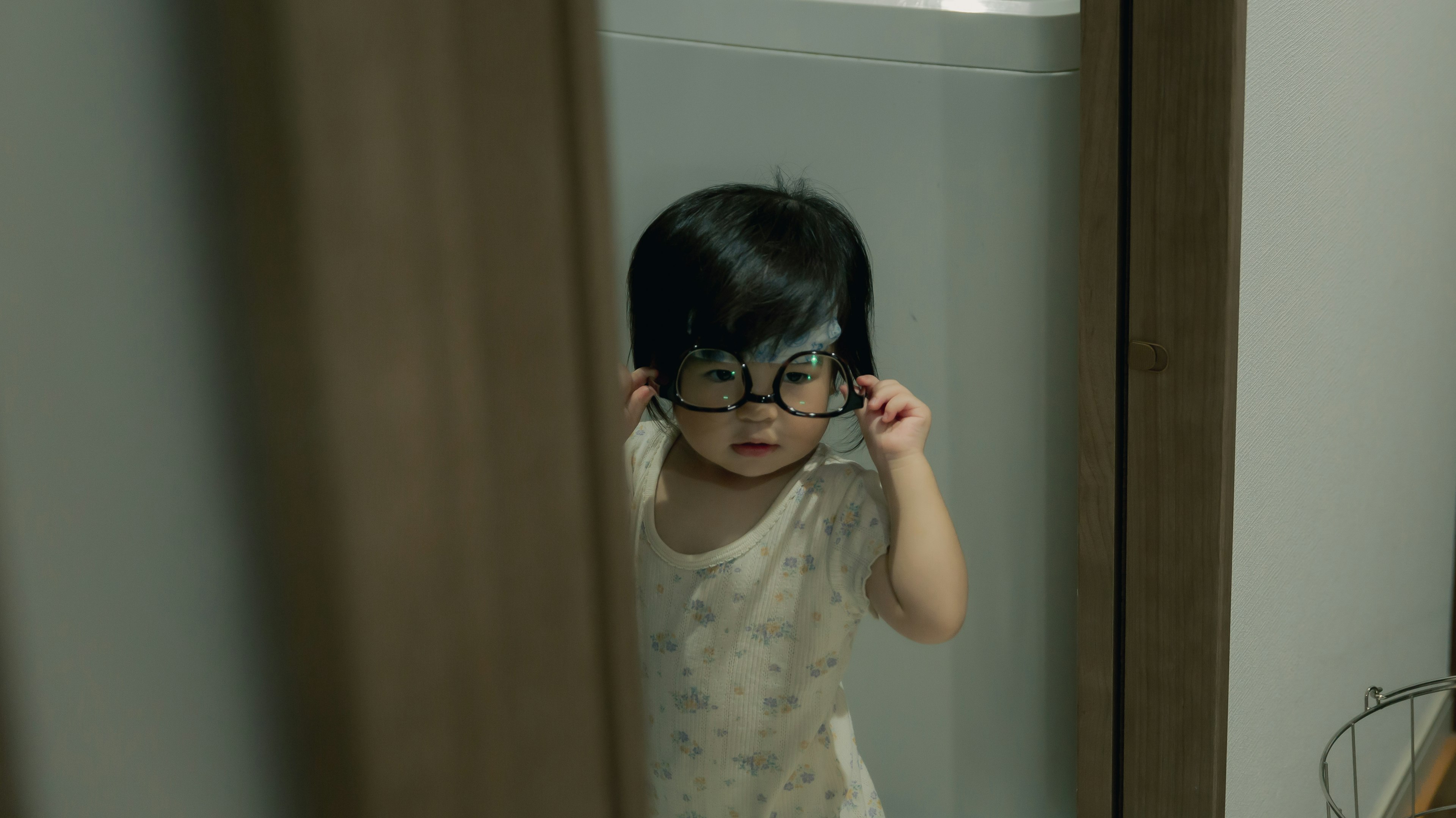 A young child adjusting glasses in front of a mirror