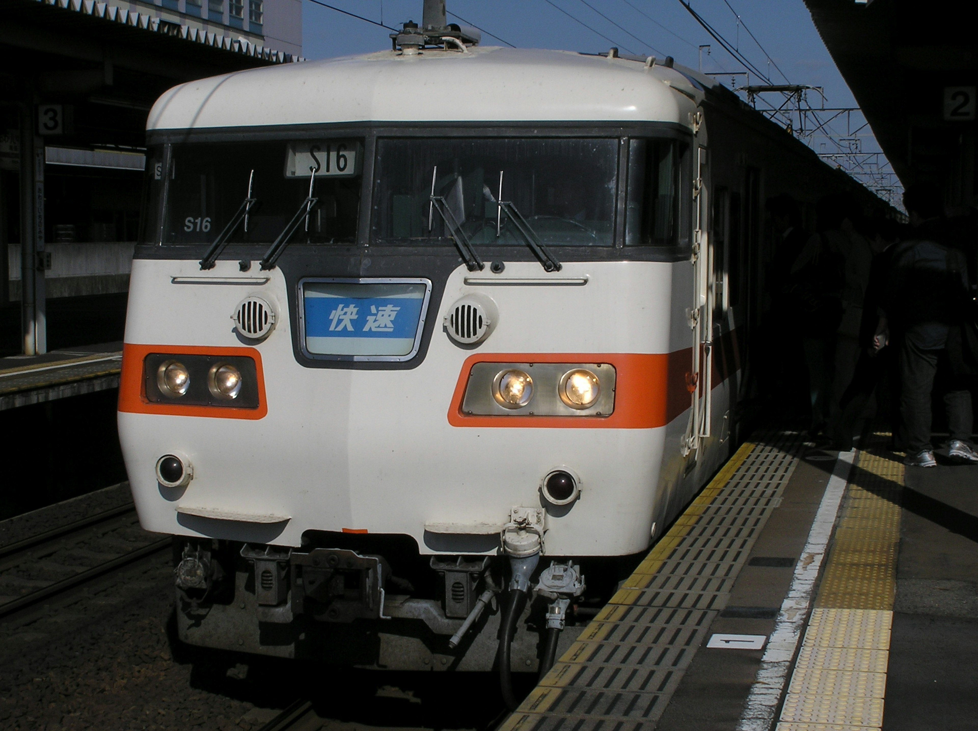 Tren japonés con esquema de color naranja y blanco llegando a una estación