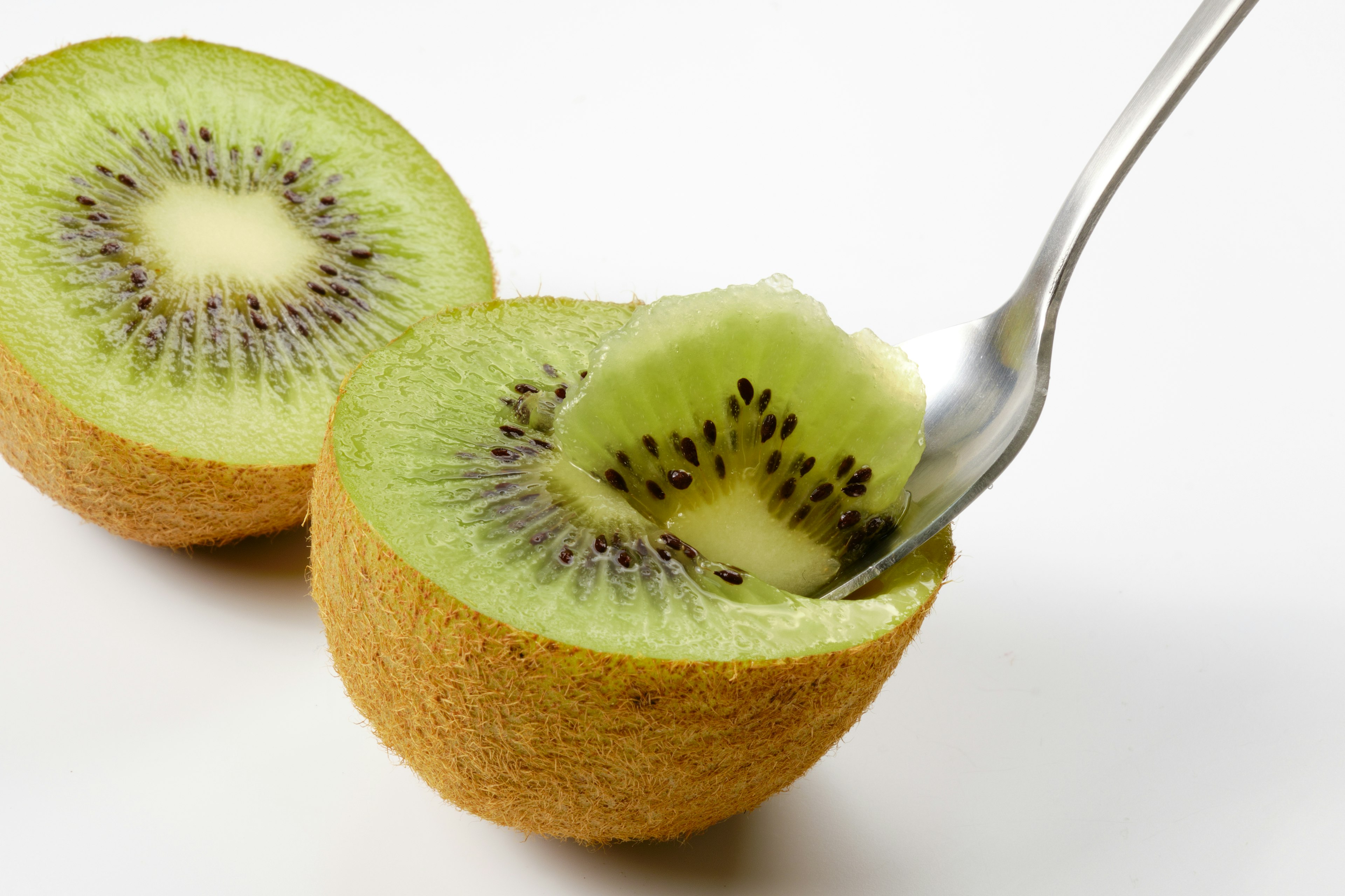 Setengah kiwi dengan sendok yang menggali daging hijau