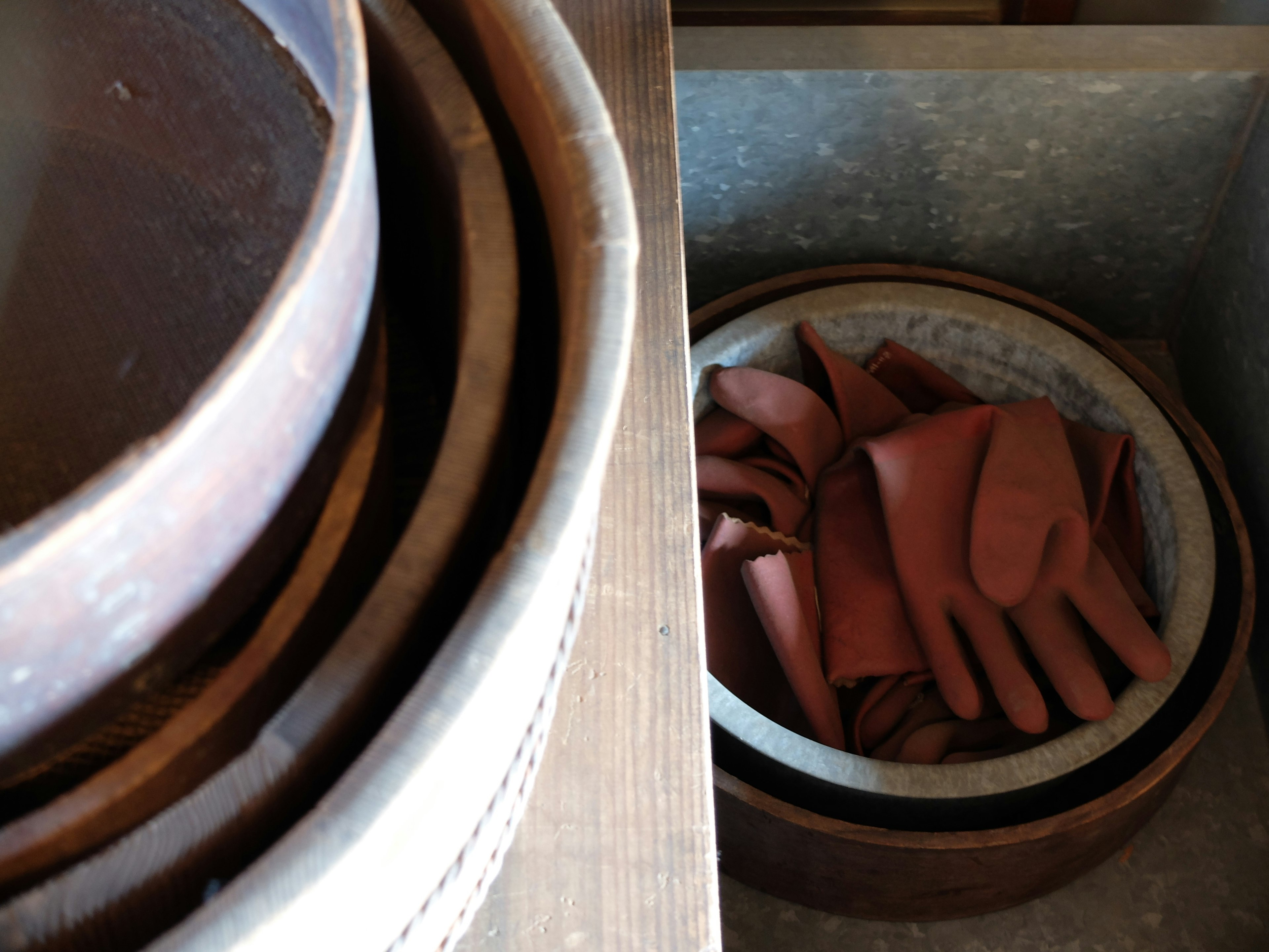 Platos de madera apilados junto a un recipiente con guantes rojos