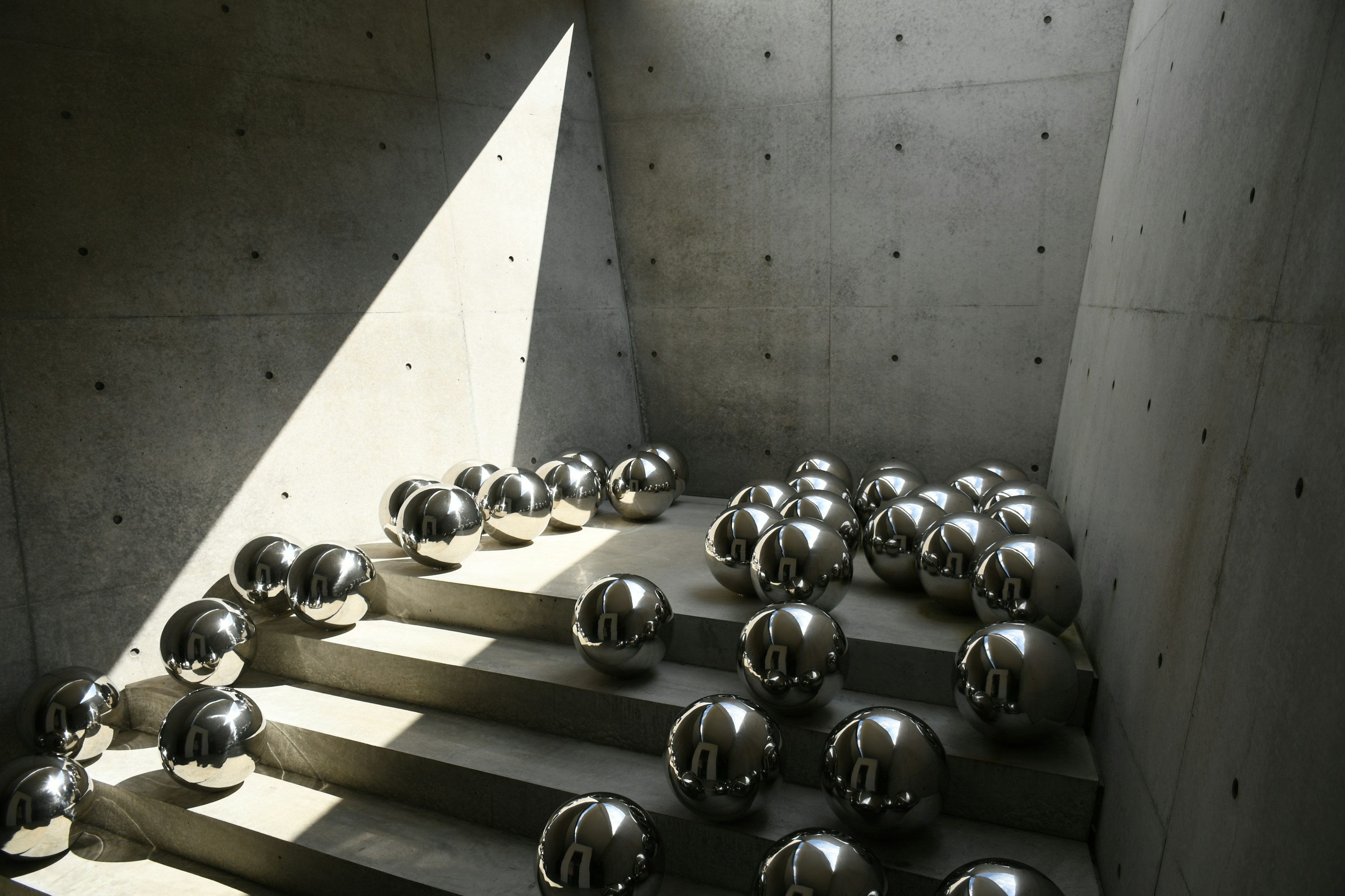 Silver spheres scattered on stairs with striking light hitting concrete walls