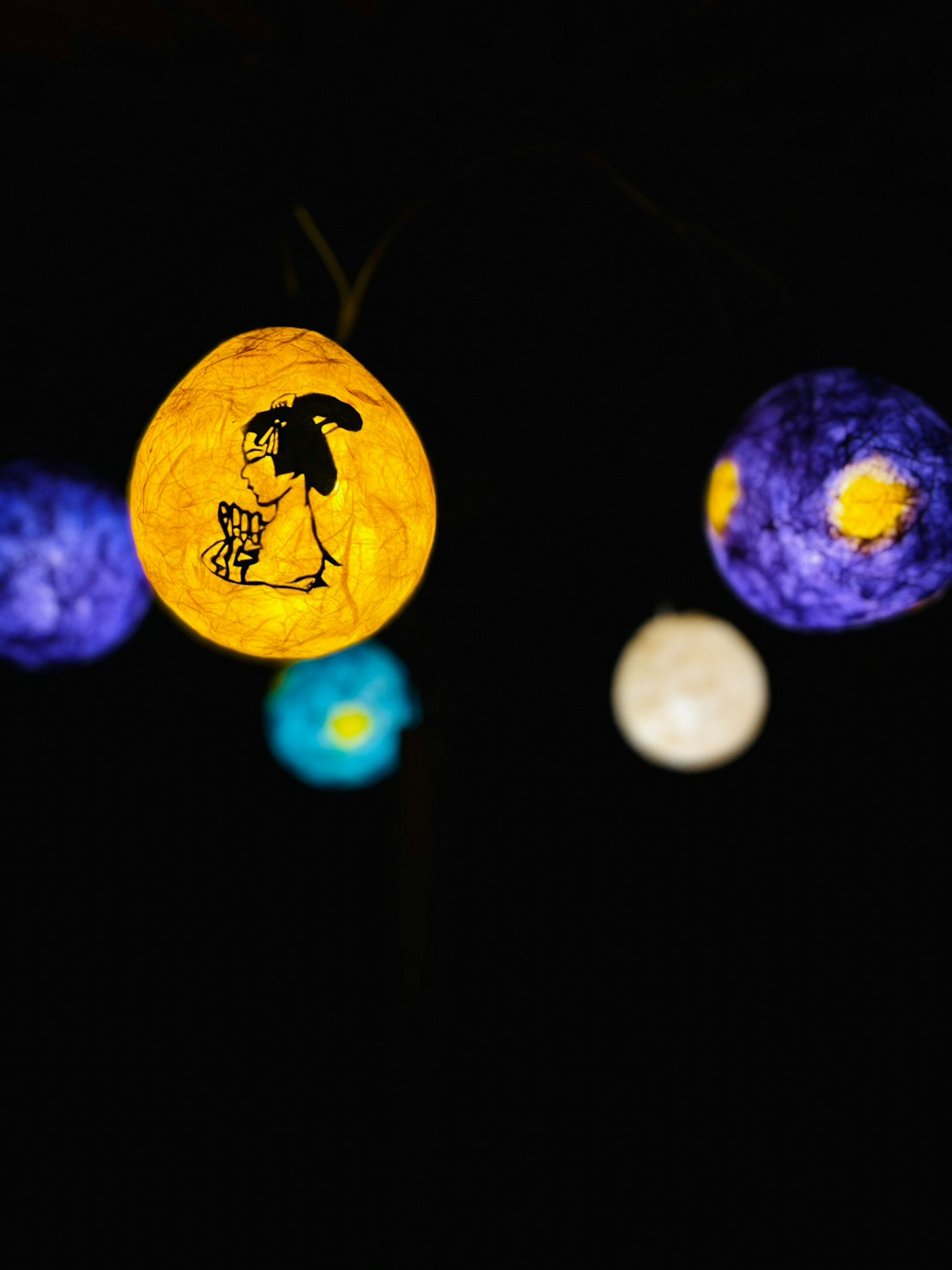 Lanternes décoratives colorées sur fond noir avec une lanterne jaune illustrant une femme et un chat