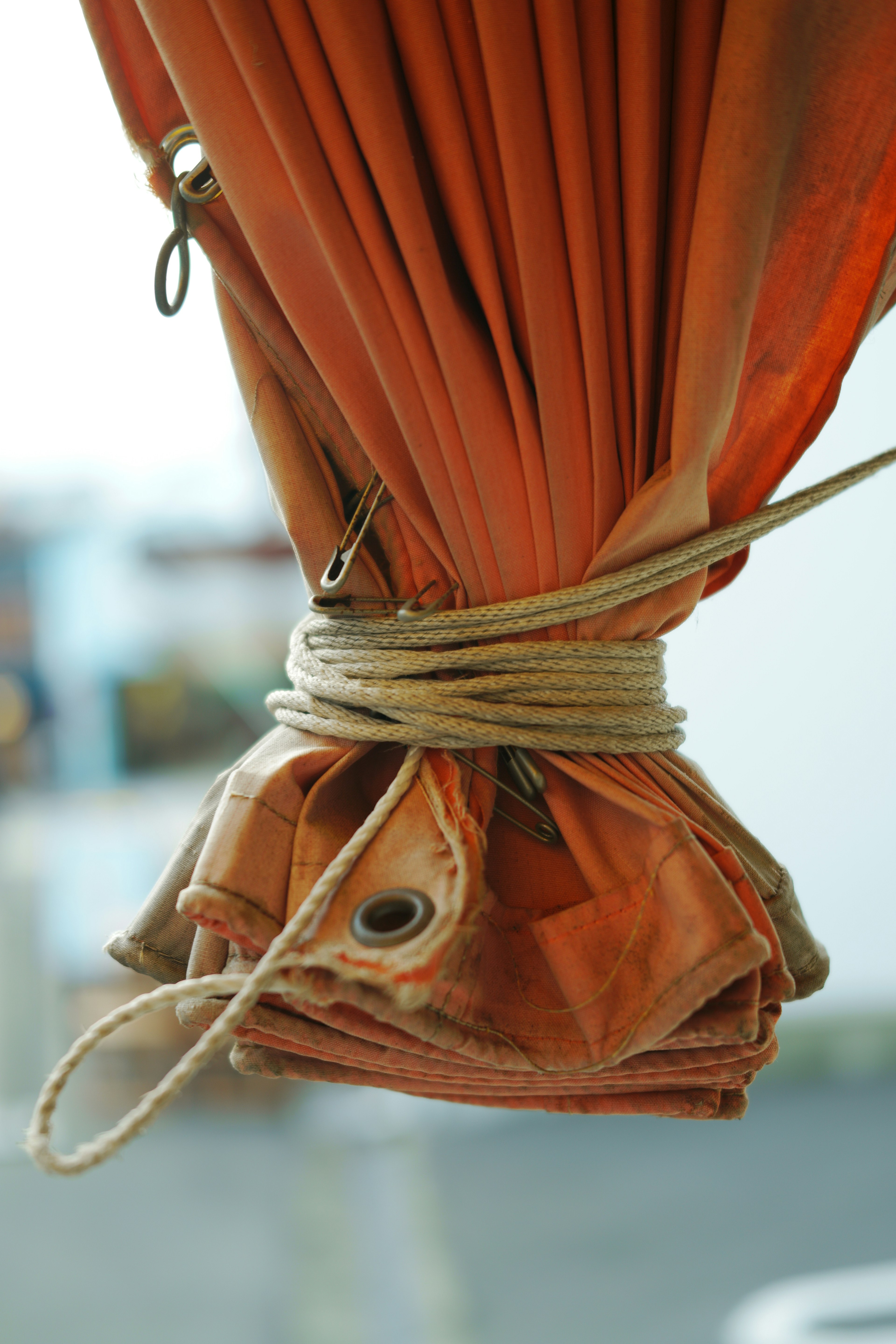 Close-up of tied orange curtain with visible grommet and rope