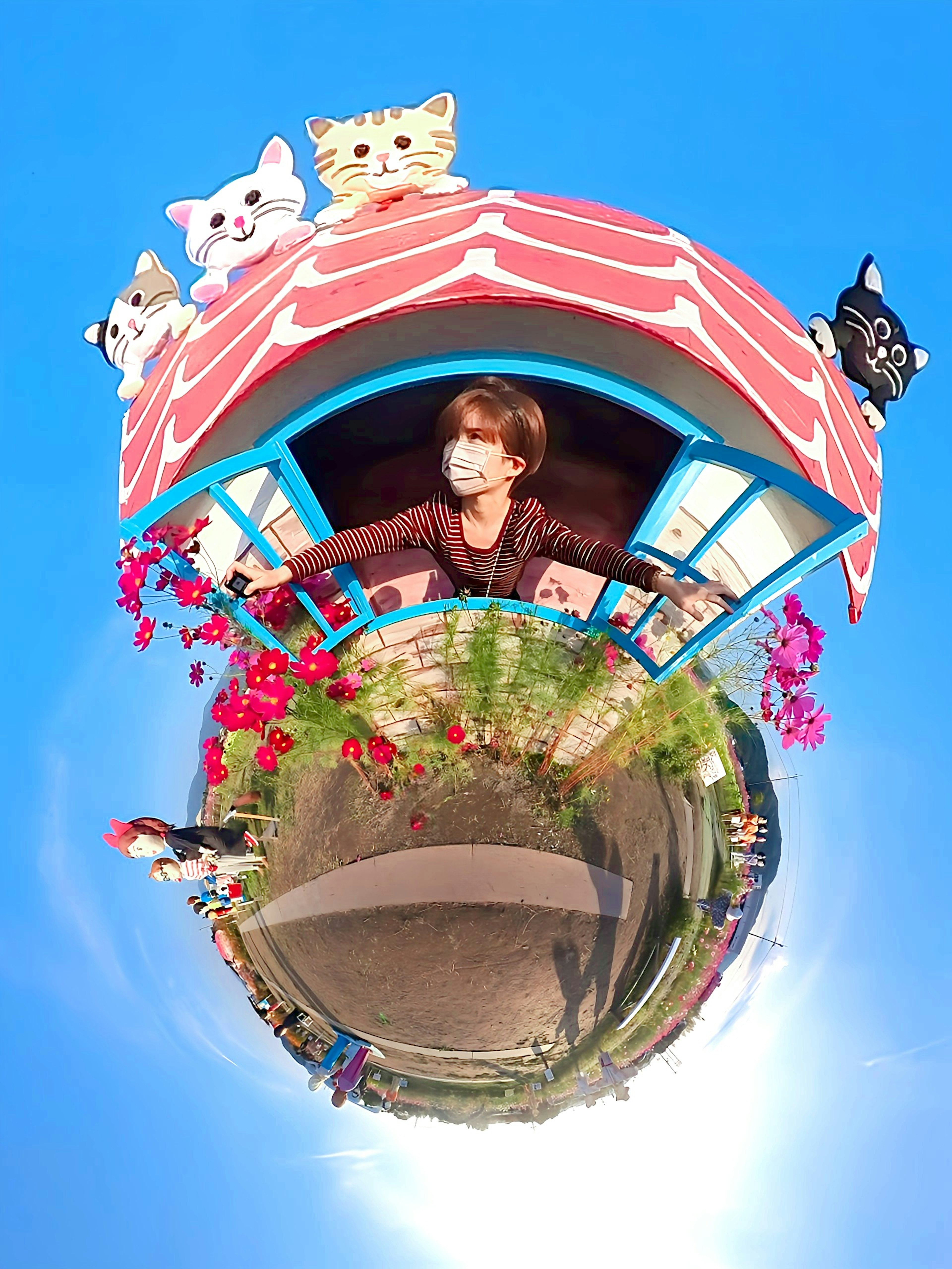 A woman peeking out from a colorful cabin adorned with cat decorations under a blue sky