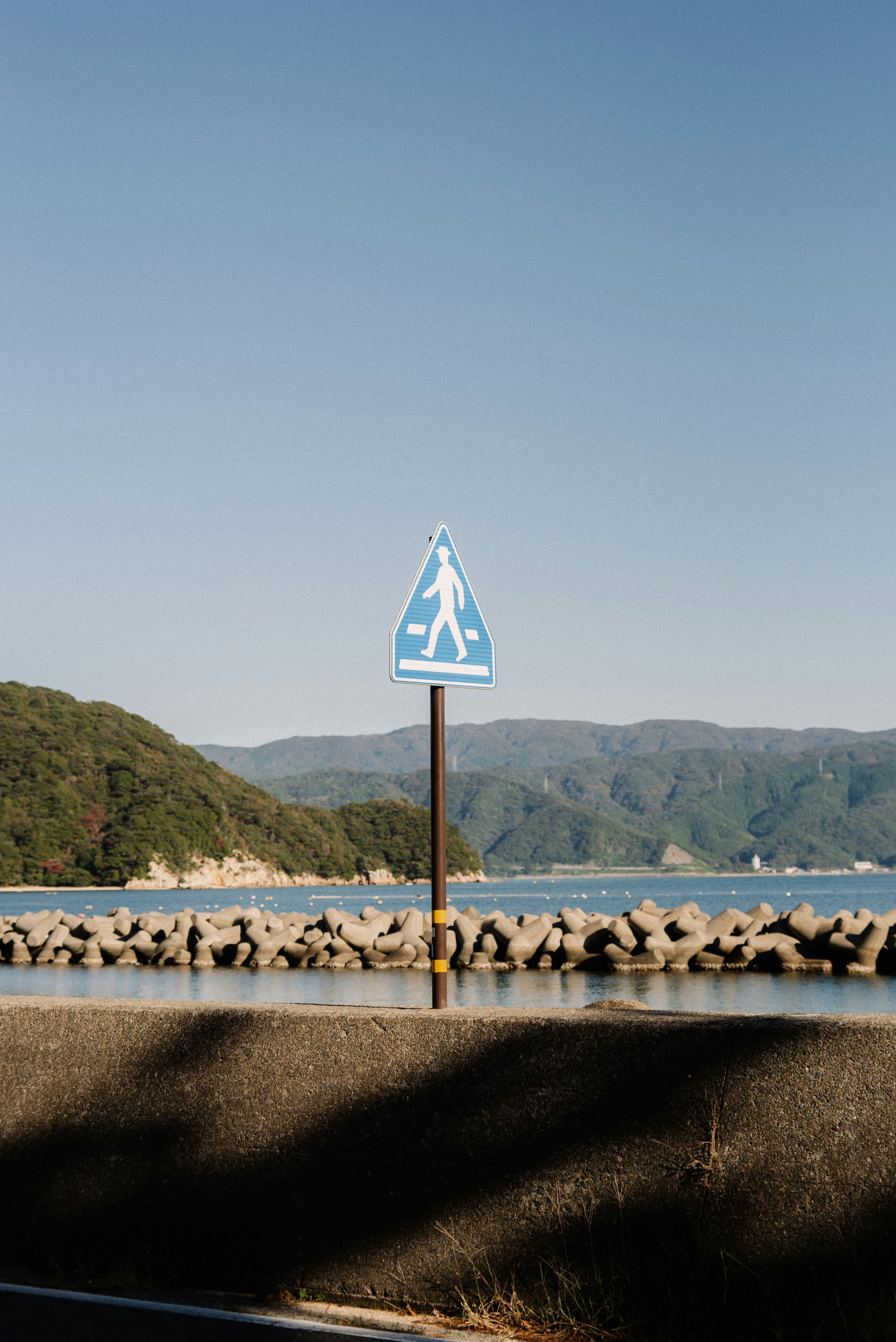 Blaues Fußgängerschild steht nahe dem Meer mit Bergen im Hintergrund