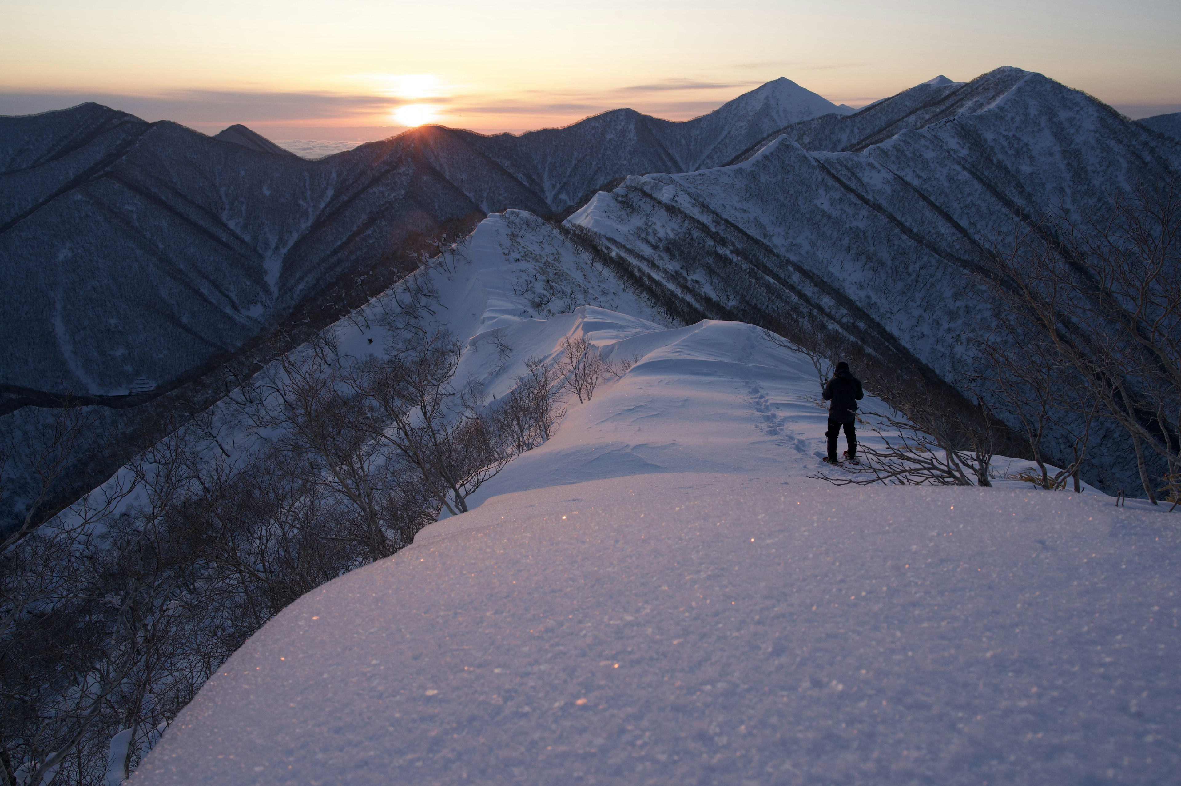 雪に覆われた山の稜線に立つハイカーと夕日