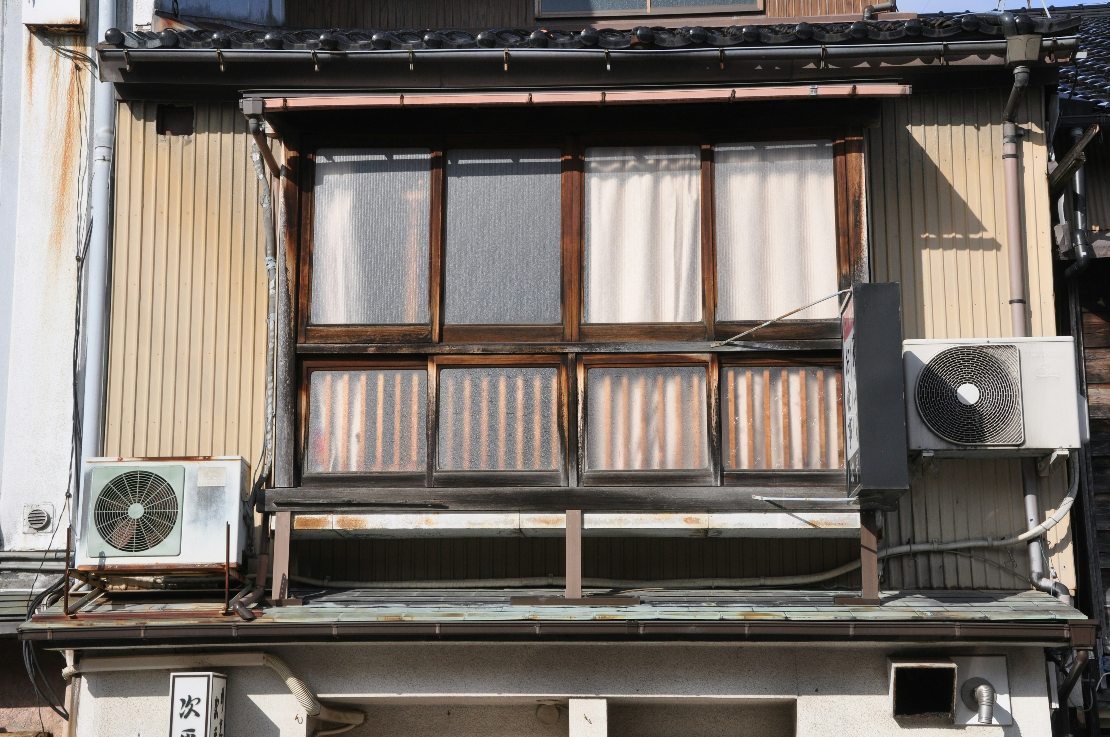 Exterior de una antigua casa japonesa con una ventana y unidades de aire acondicionado