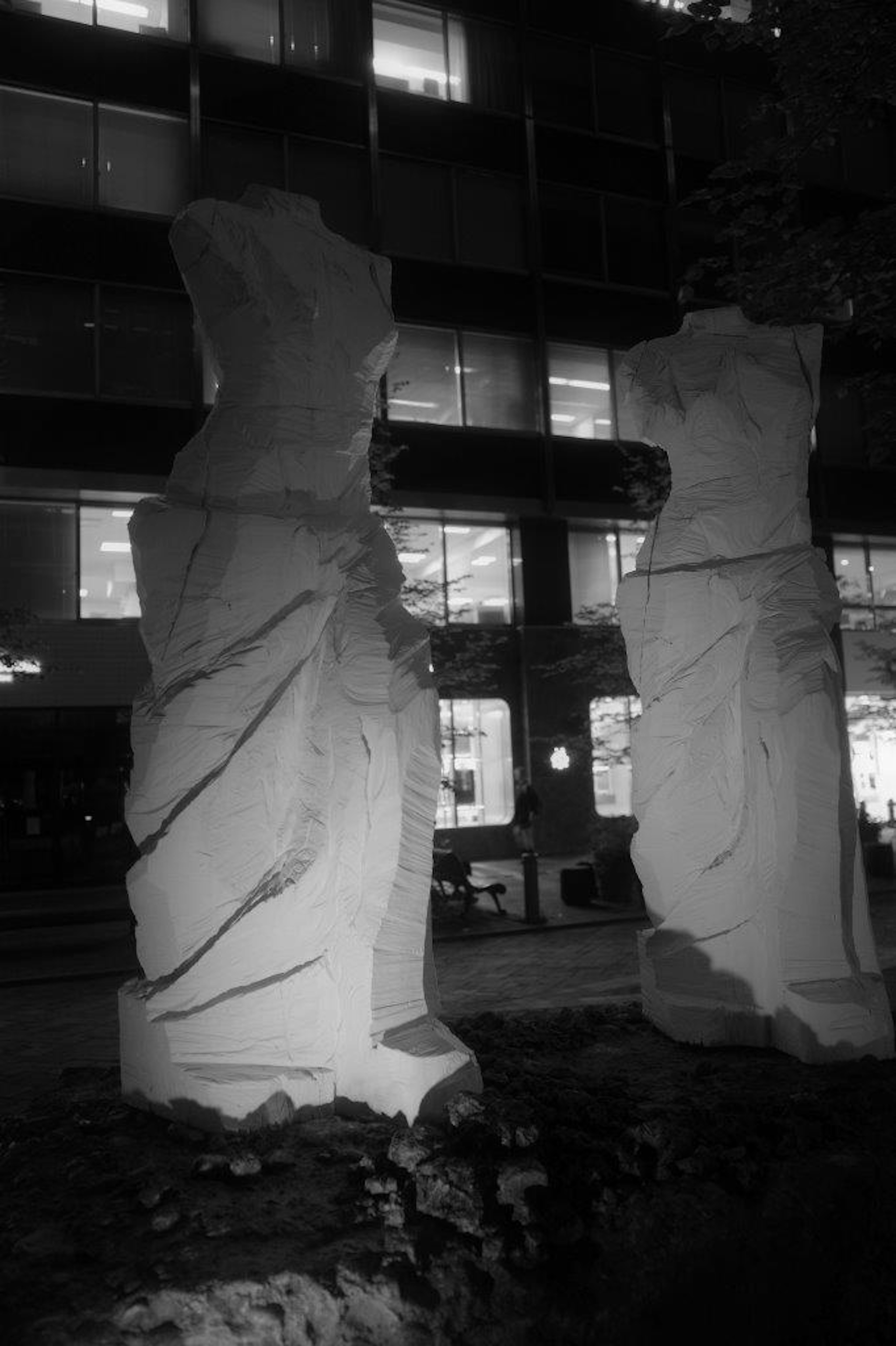 Dos esculturas blancas de pie en un entorno urbano por la noche