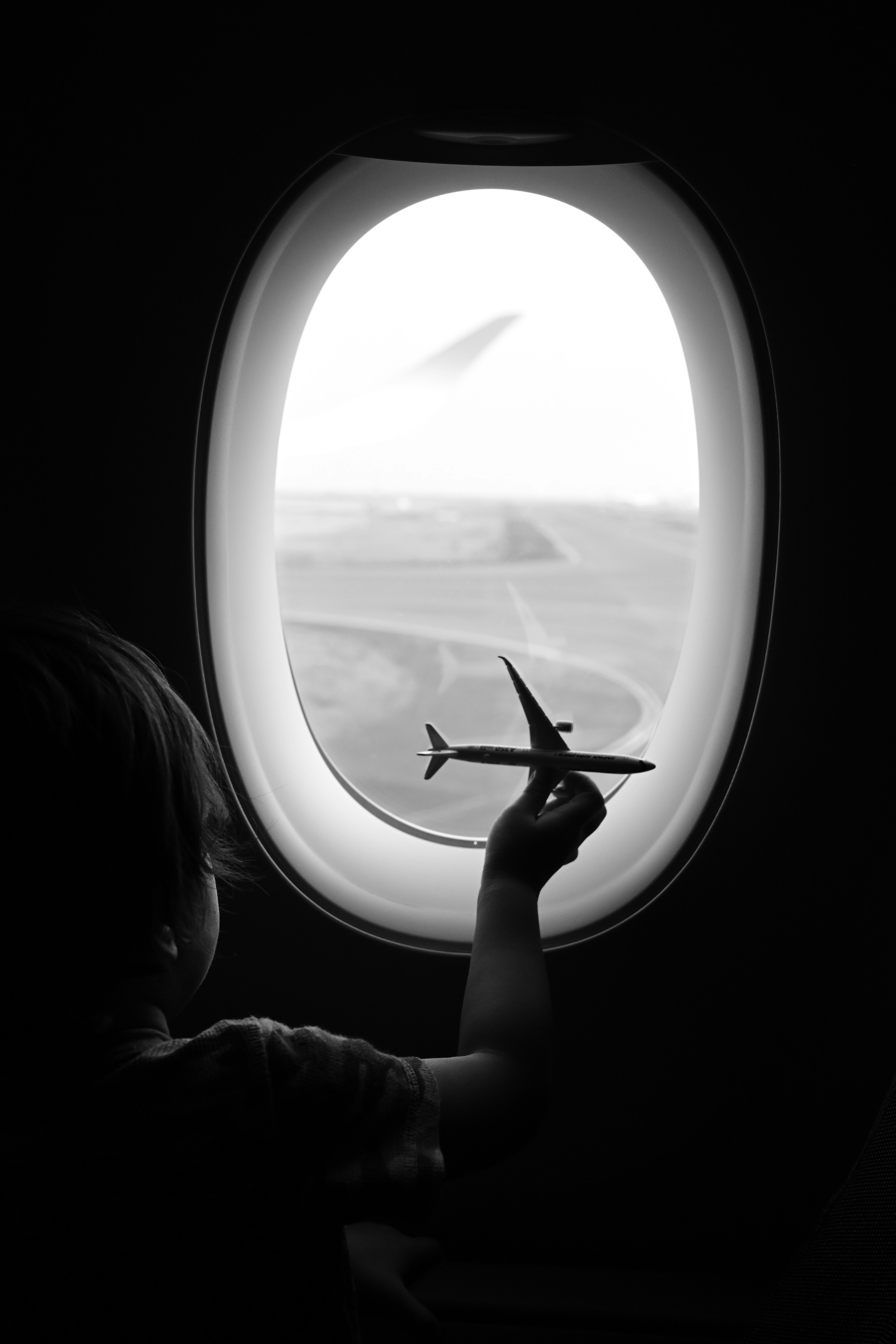 Kind schaut aus dem Flugzeugfenster und hält ein Spielzeugflugzeug