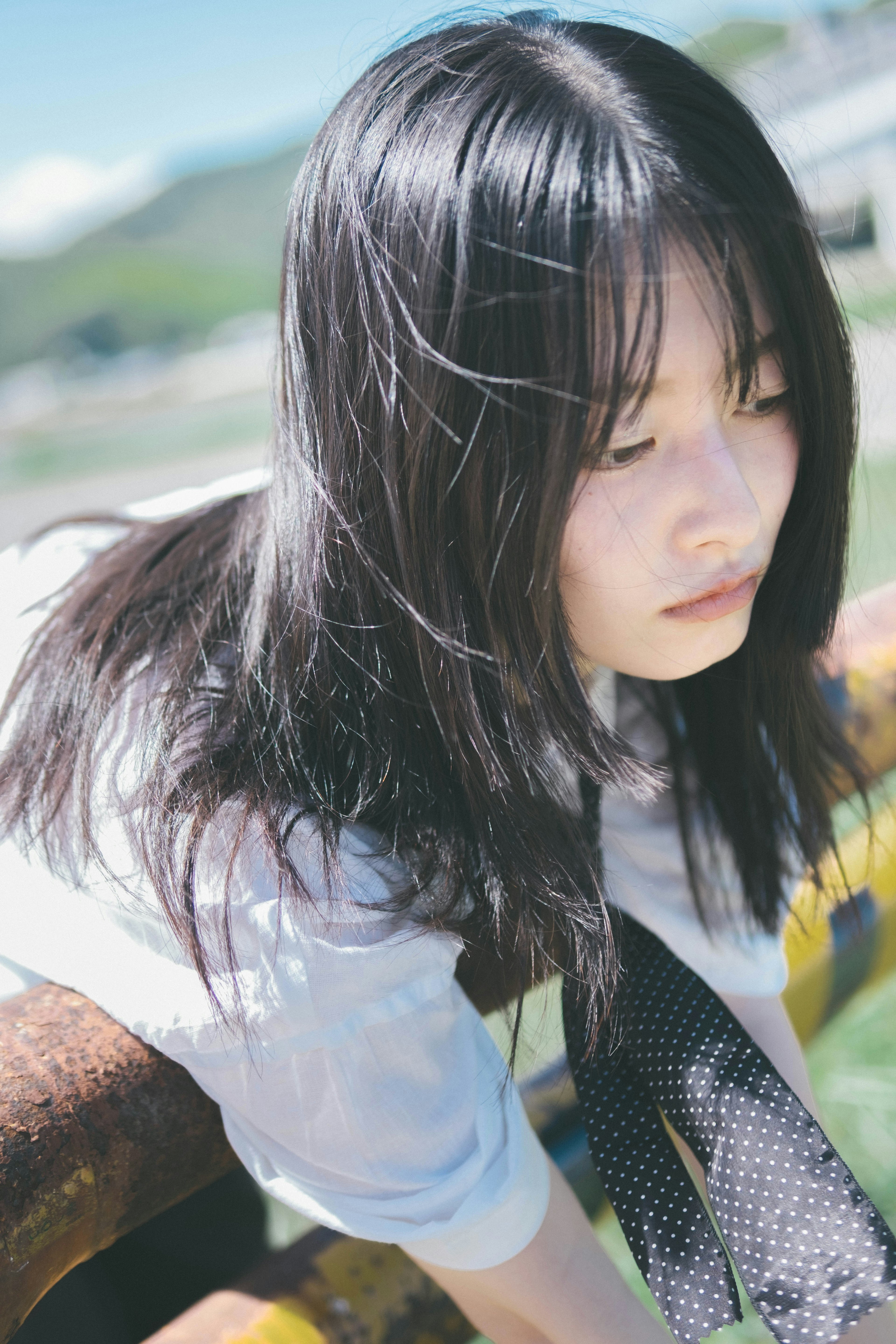 Portrait of a young woman leaning against a fence under a blue sky