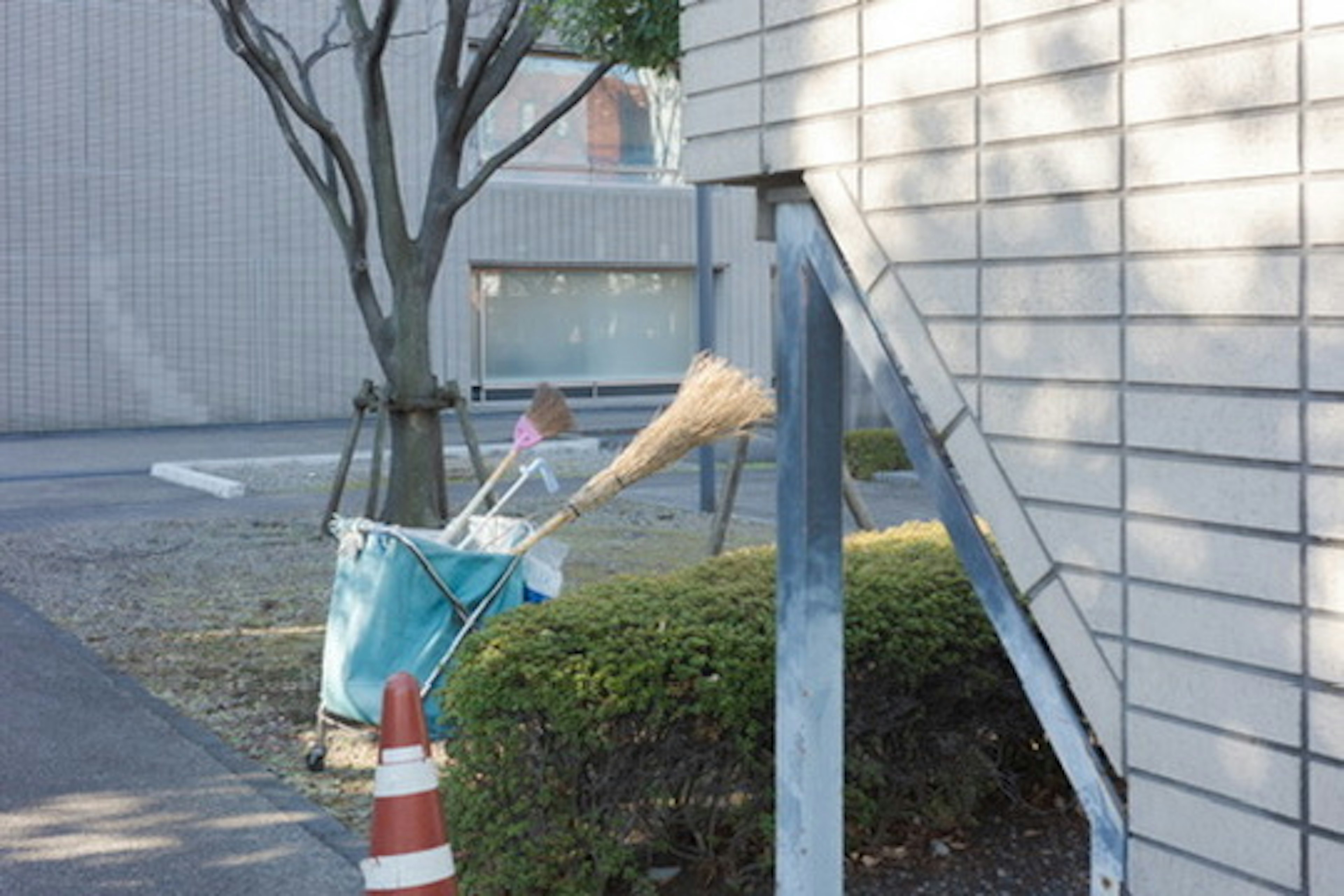 A blue bucket with cleaning tools and a broom leaning against a wall