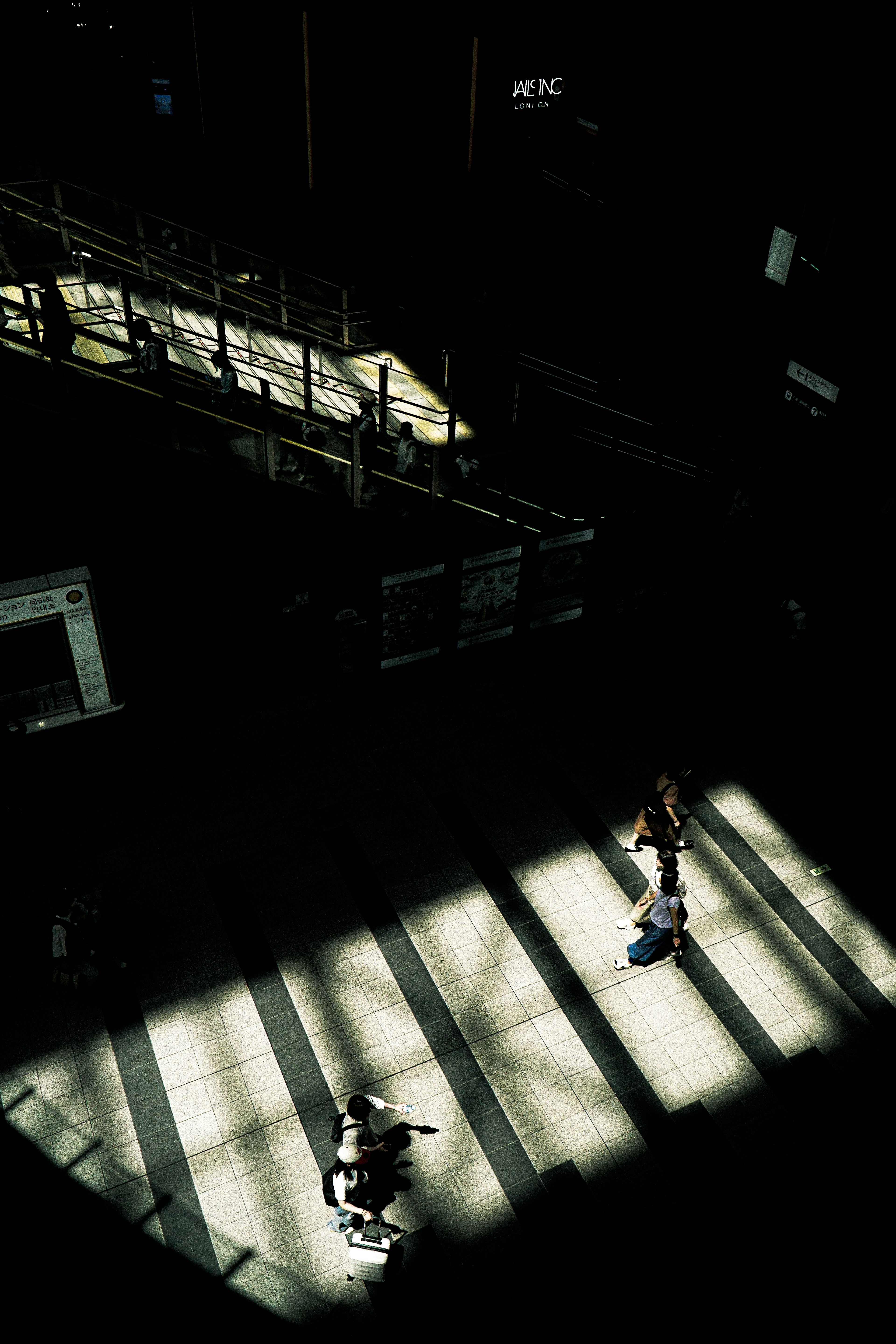 Silhouettes de personnes marchant dans un espace sombre éclairé par des rayons de lumière