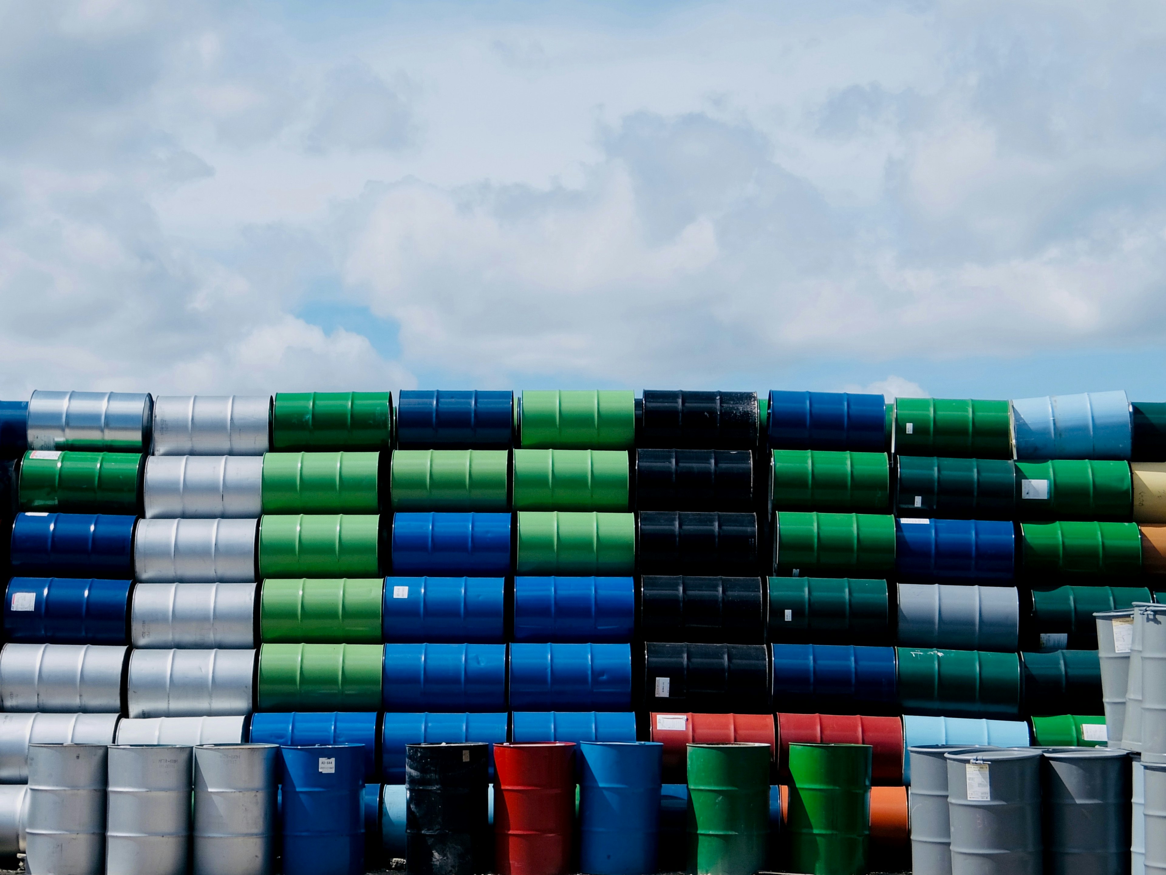 Colorful stacked barrels in various shades against a cloudy sky