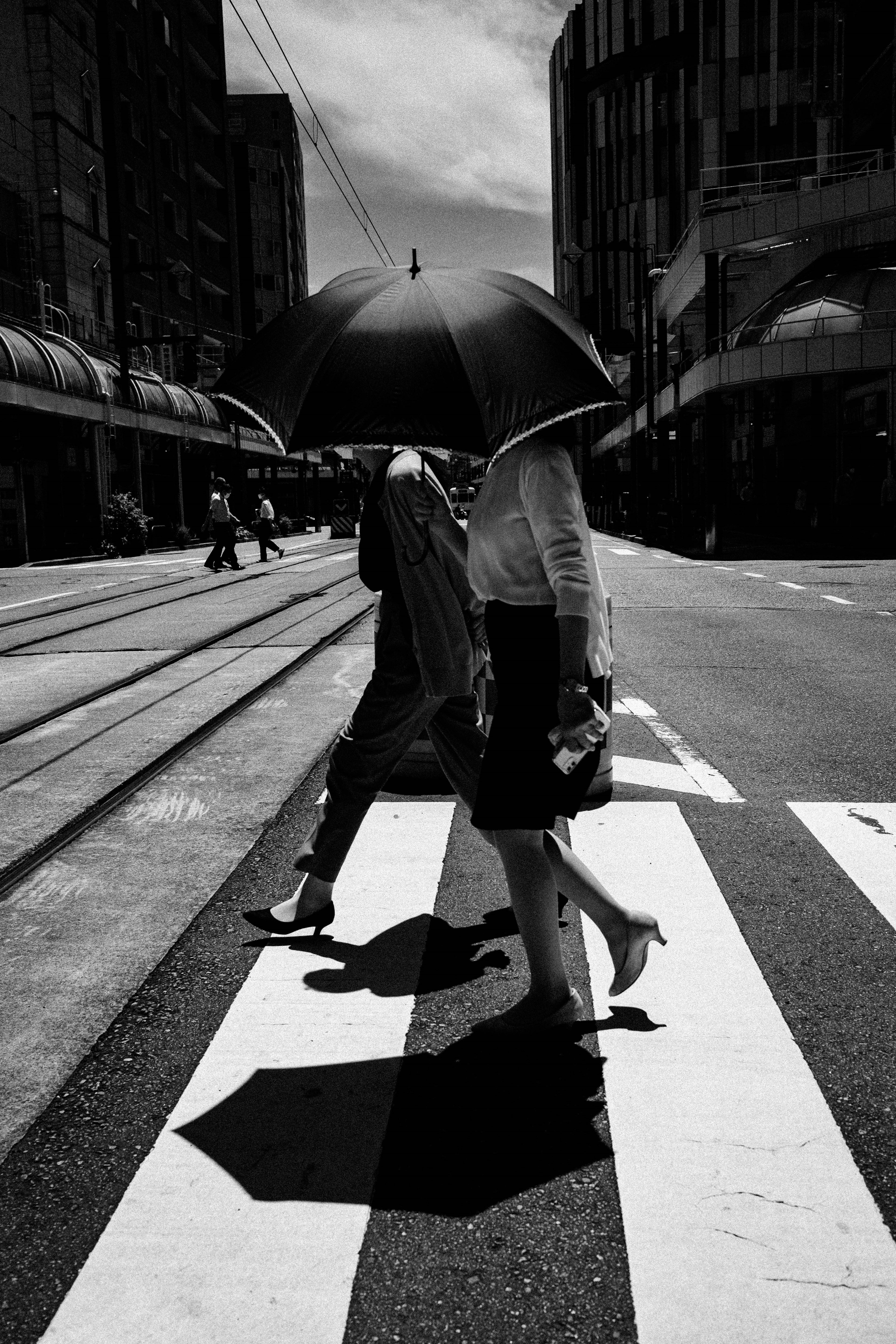 Des personnes traversant une rue avec des parapluies dans une scène urbaine en noir et blanc