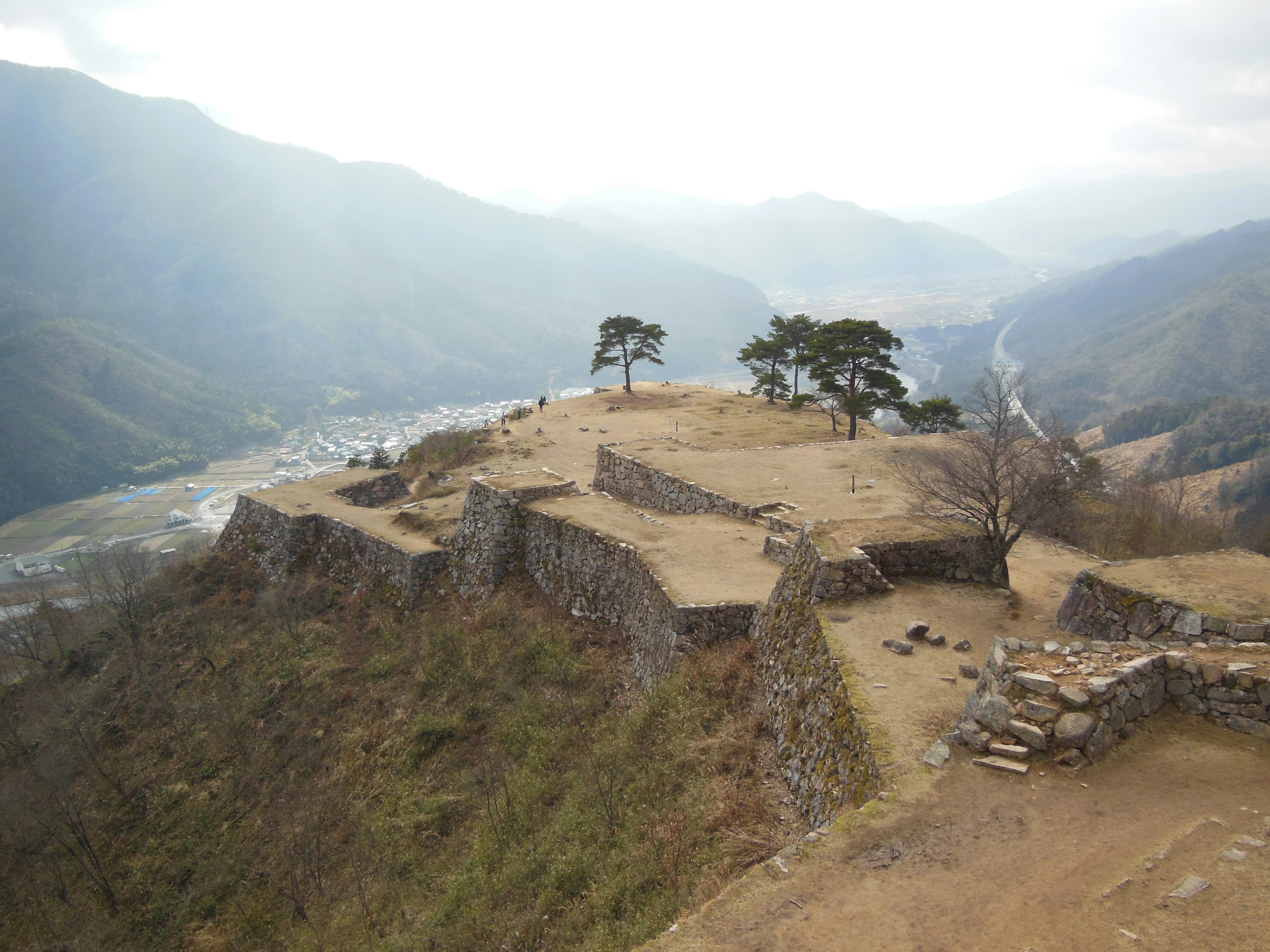 Rovine antiche su un alto plateau con montagne verdi e un fiume visibile