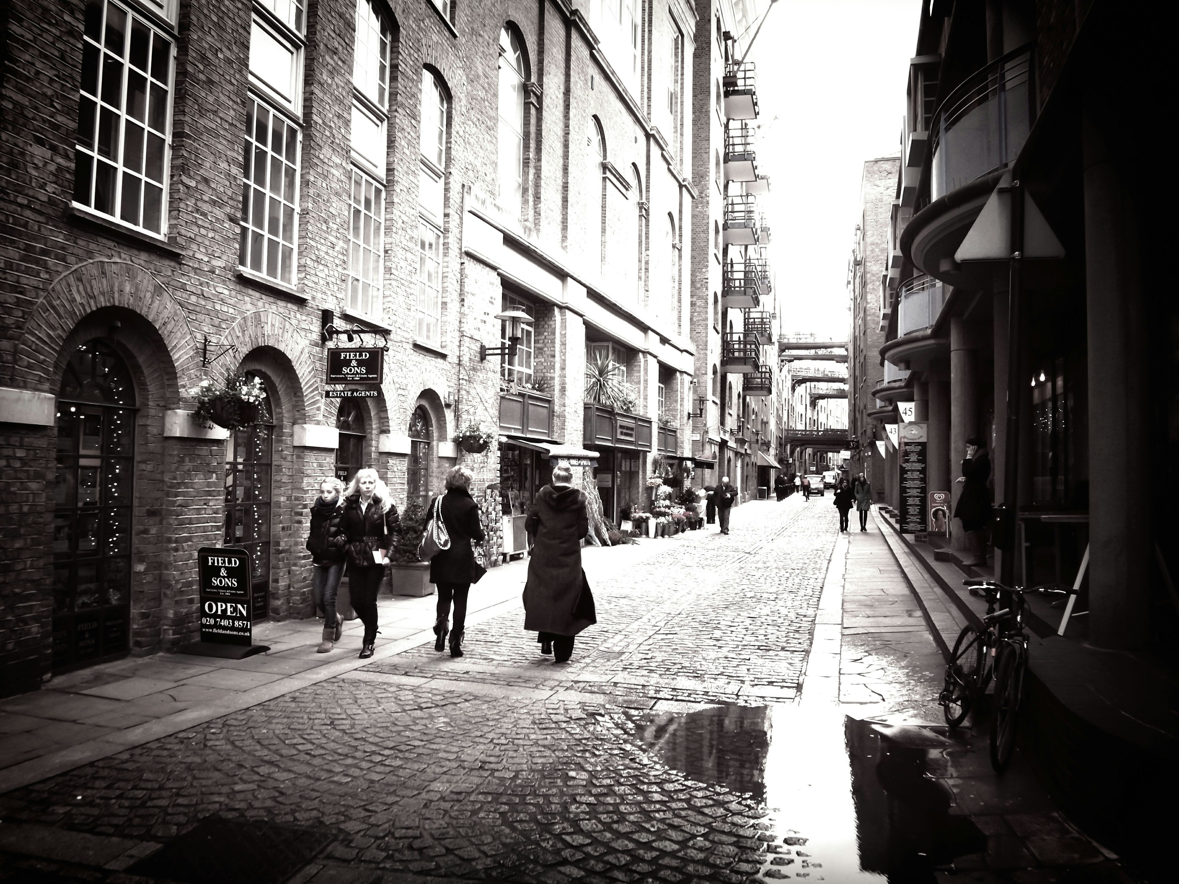 Narrow cobblestone street with people walking dimly lit buildings and shops lining the sides