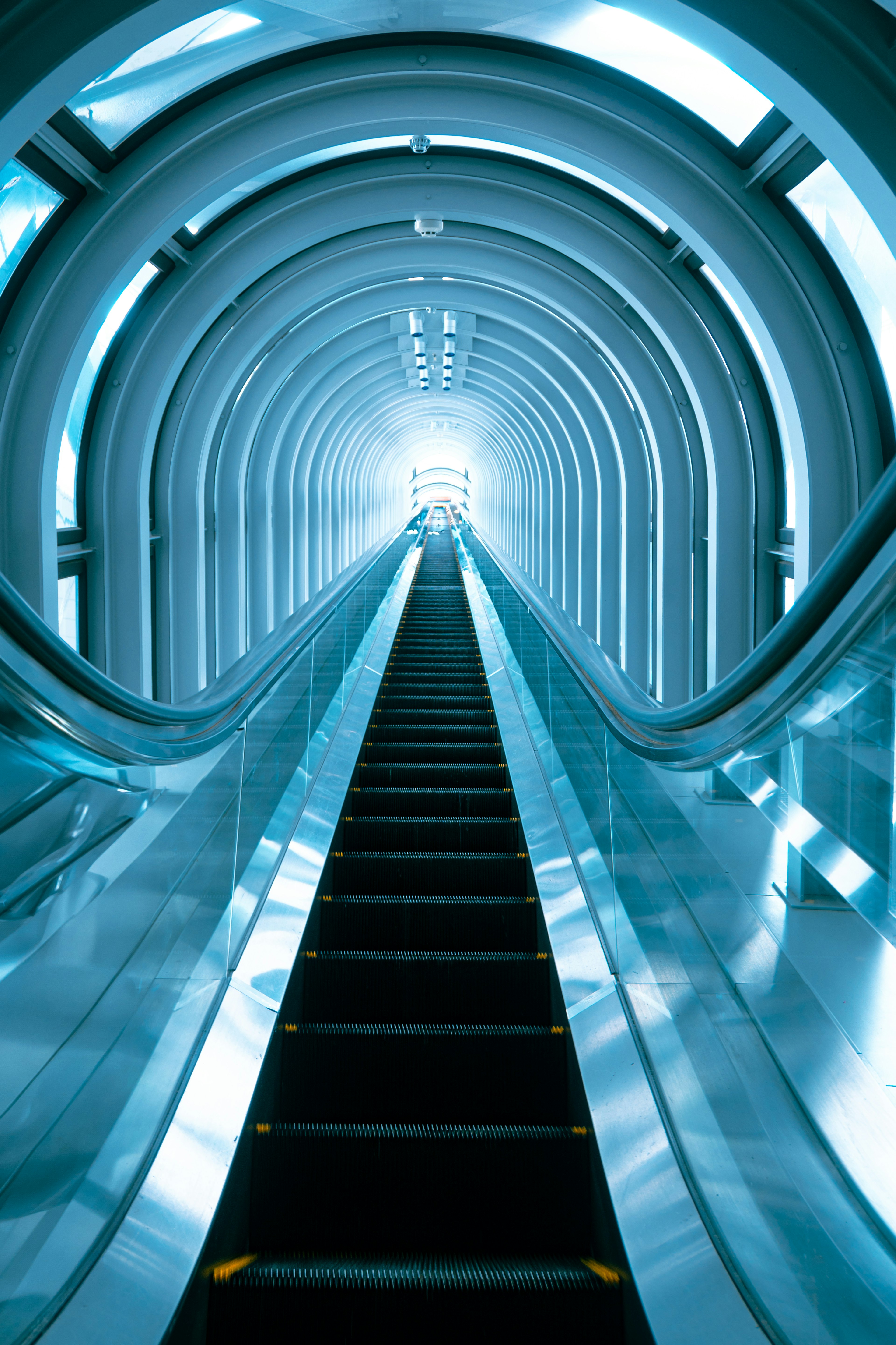 Escalier roulant montant à travers un tunnel blanc avec de la lumière au sommet