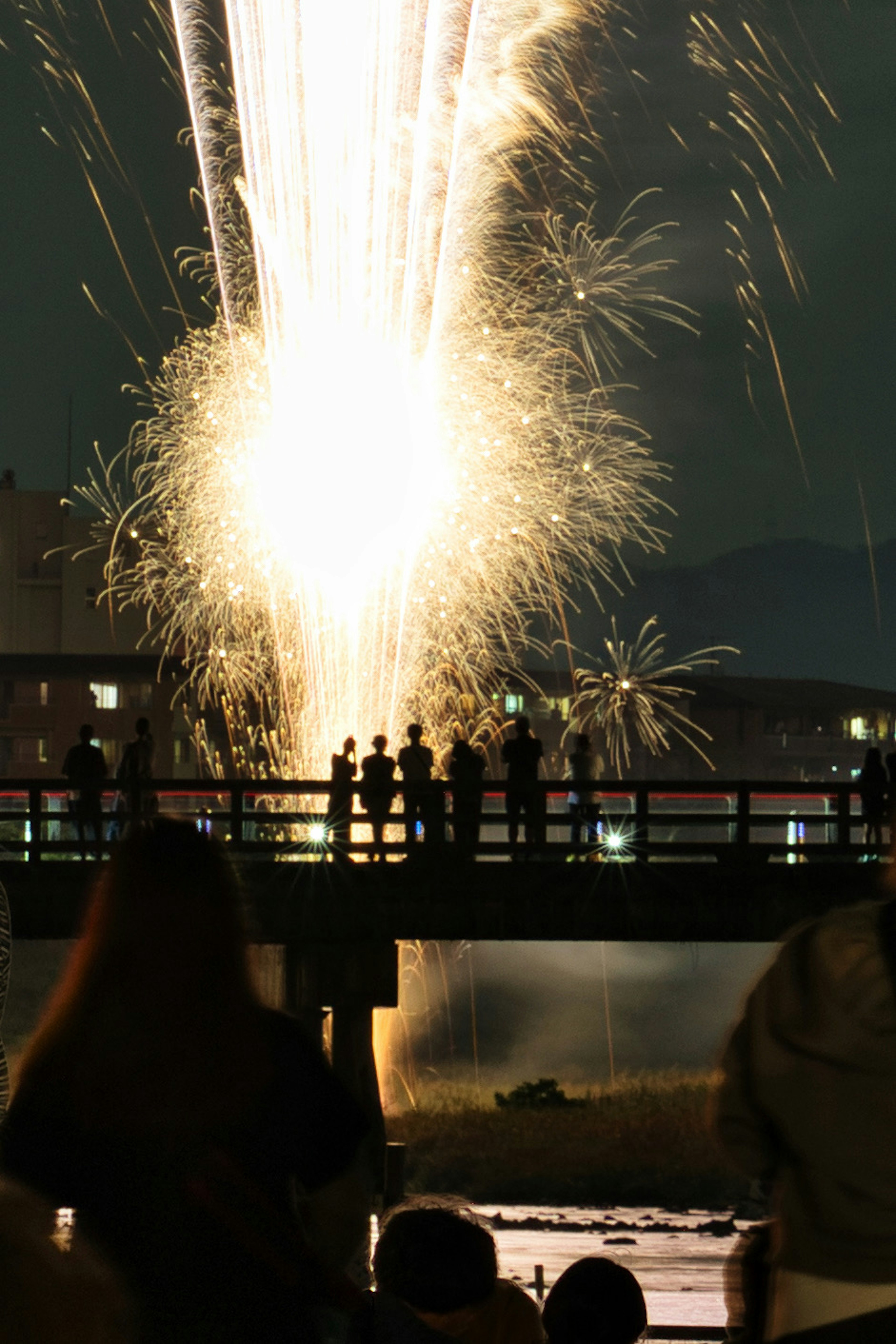 Night scene of fireworks being launched with spectators standing on a bridge