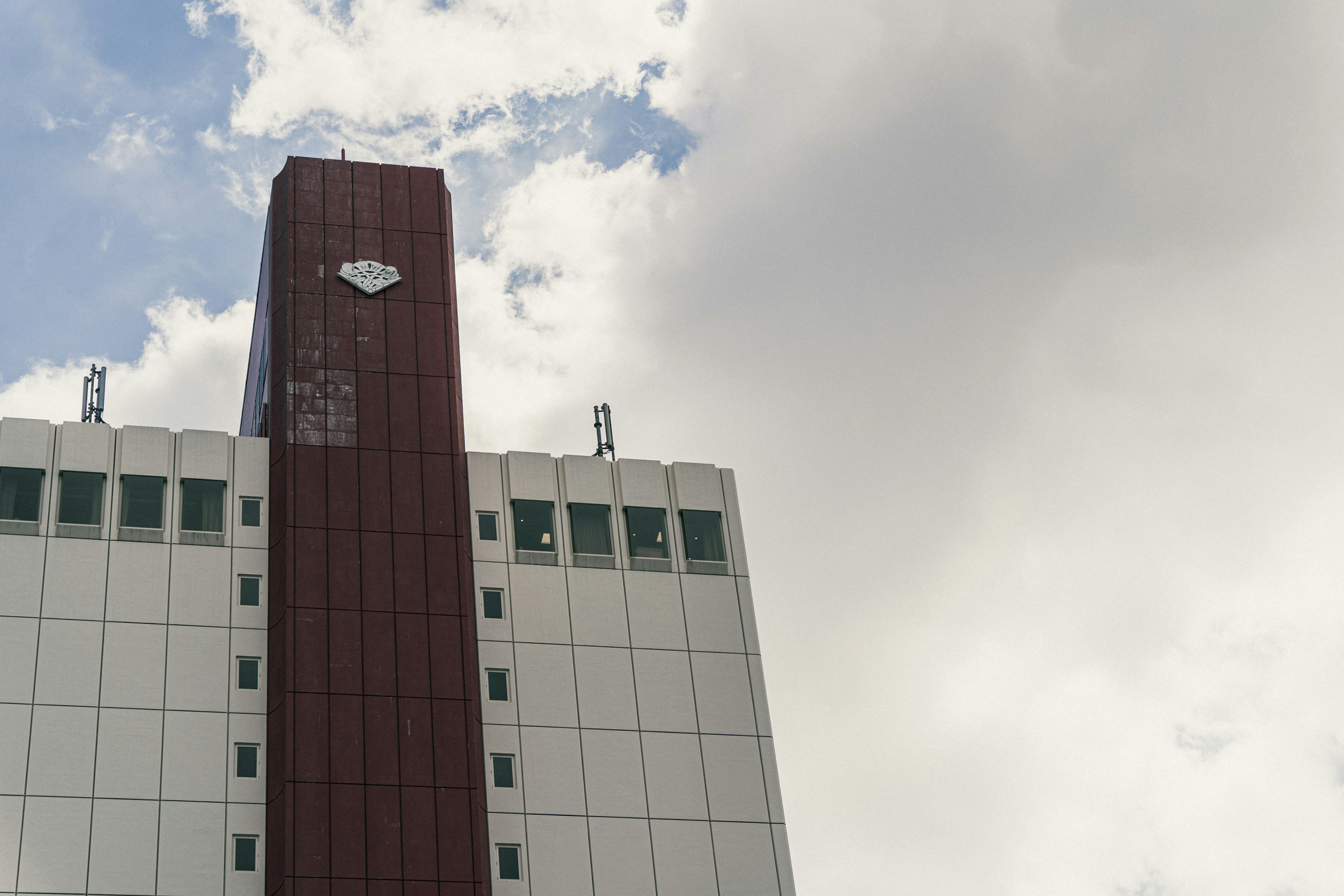 Imagen del exterior de un edificio con un logotipo en la parte superior y nubes blancas de fondo