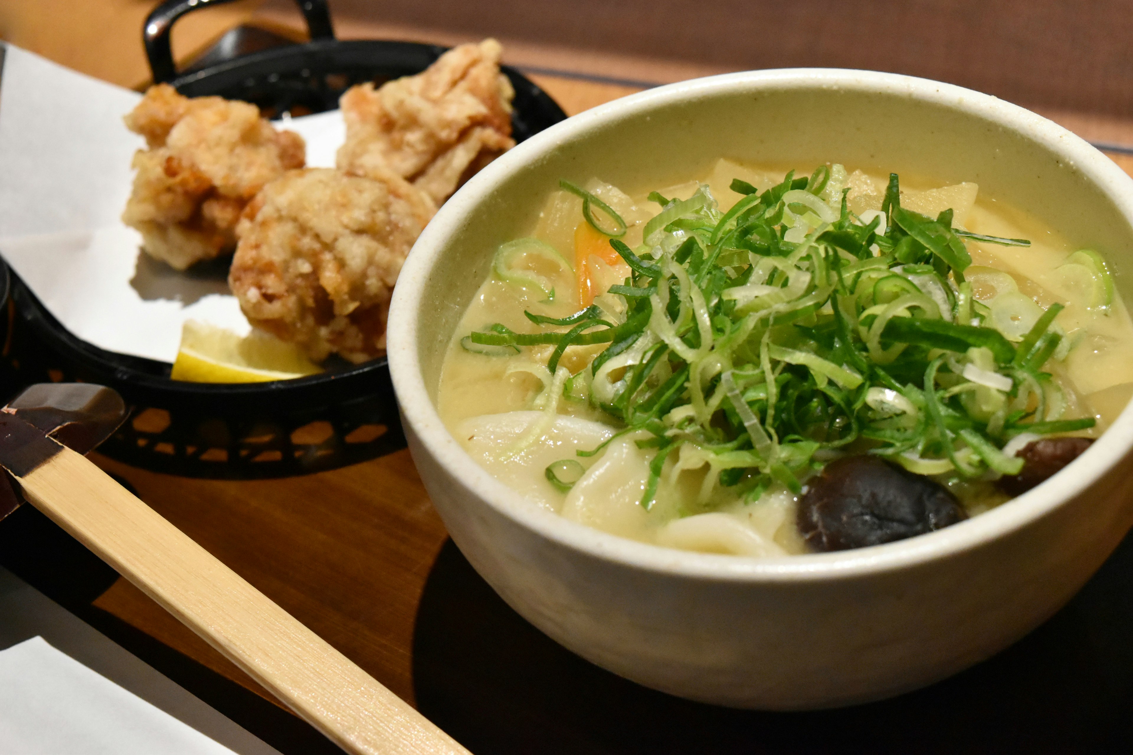 Mangkuk sup udon hangat dengan taburan daun bawang disajikan dengan ayam goreng