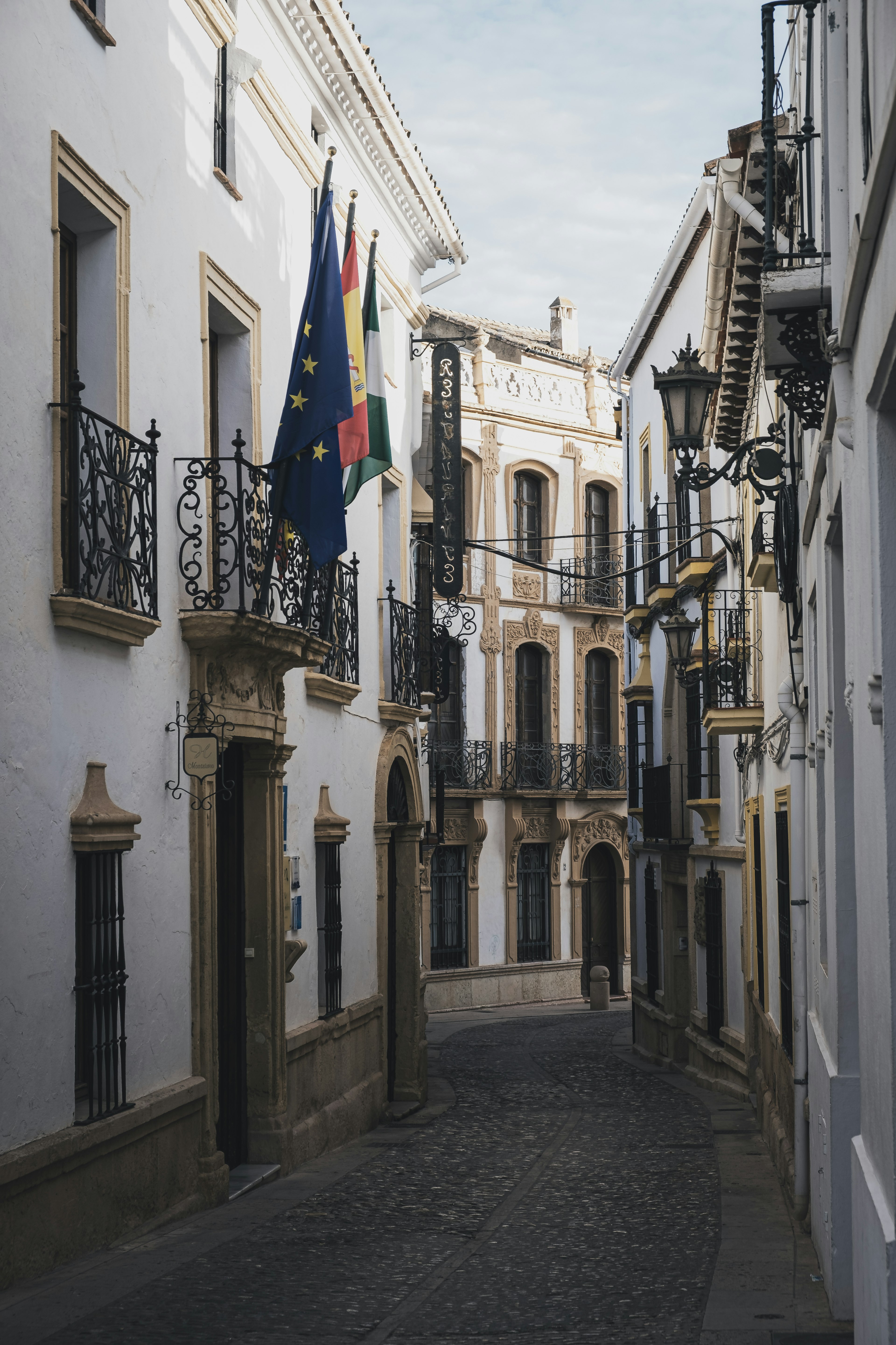 Rue étroite bordée de bâtiments blancs avec des drapeaux européens