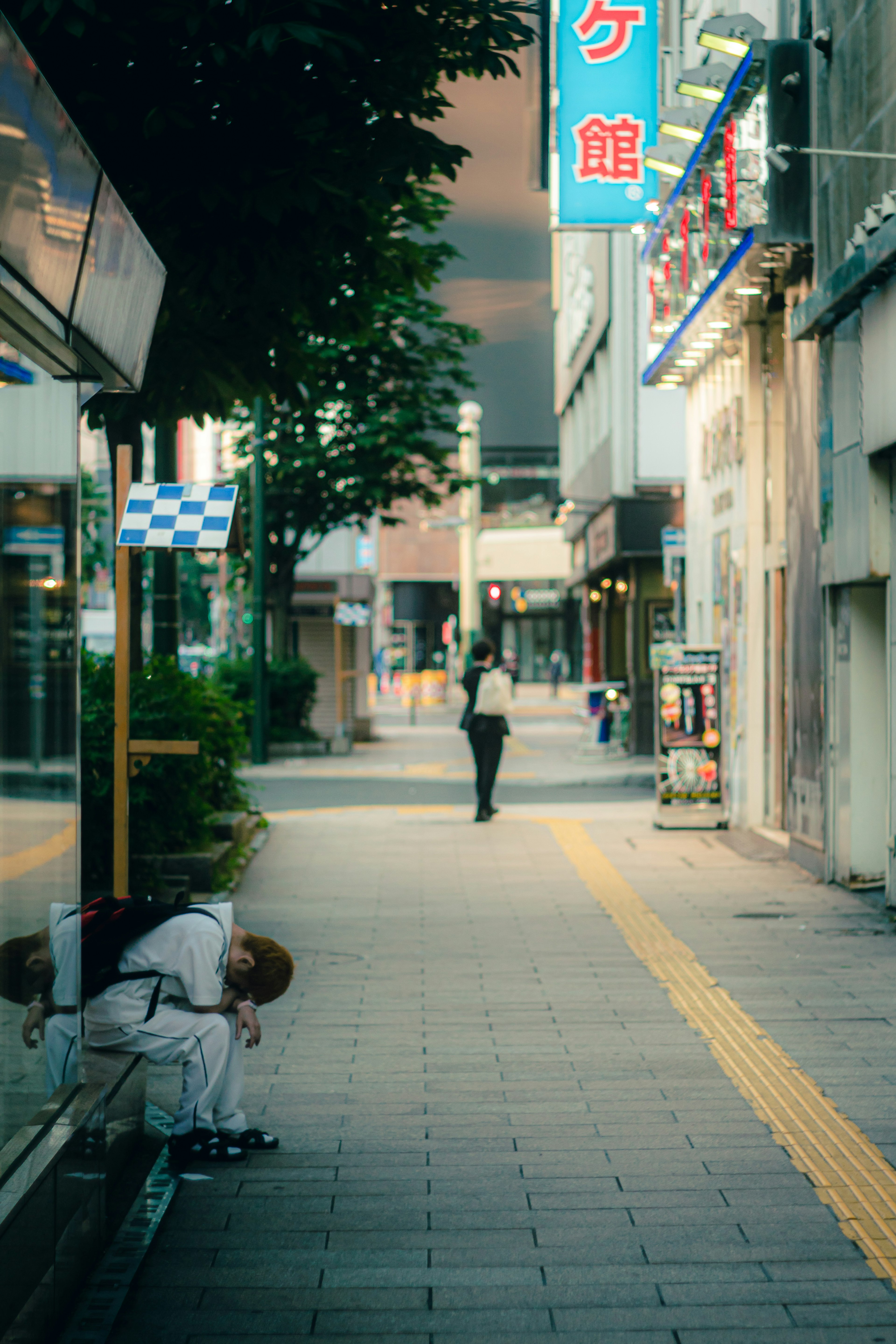 A scene of a person sitting on a sidewalk and another walking down the street