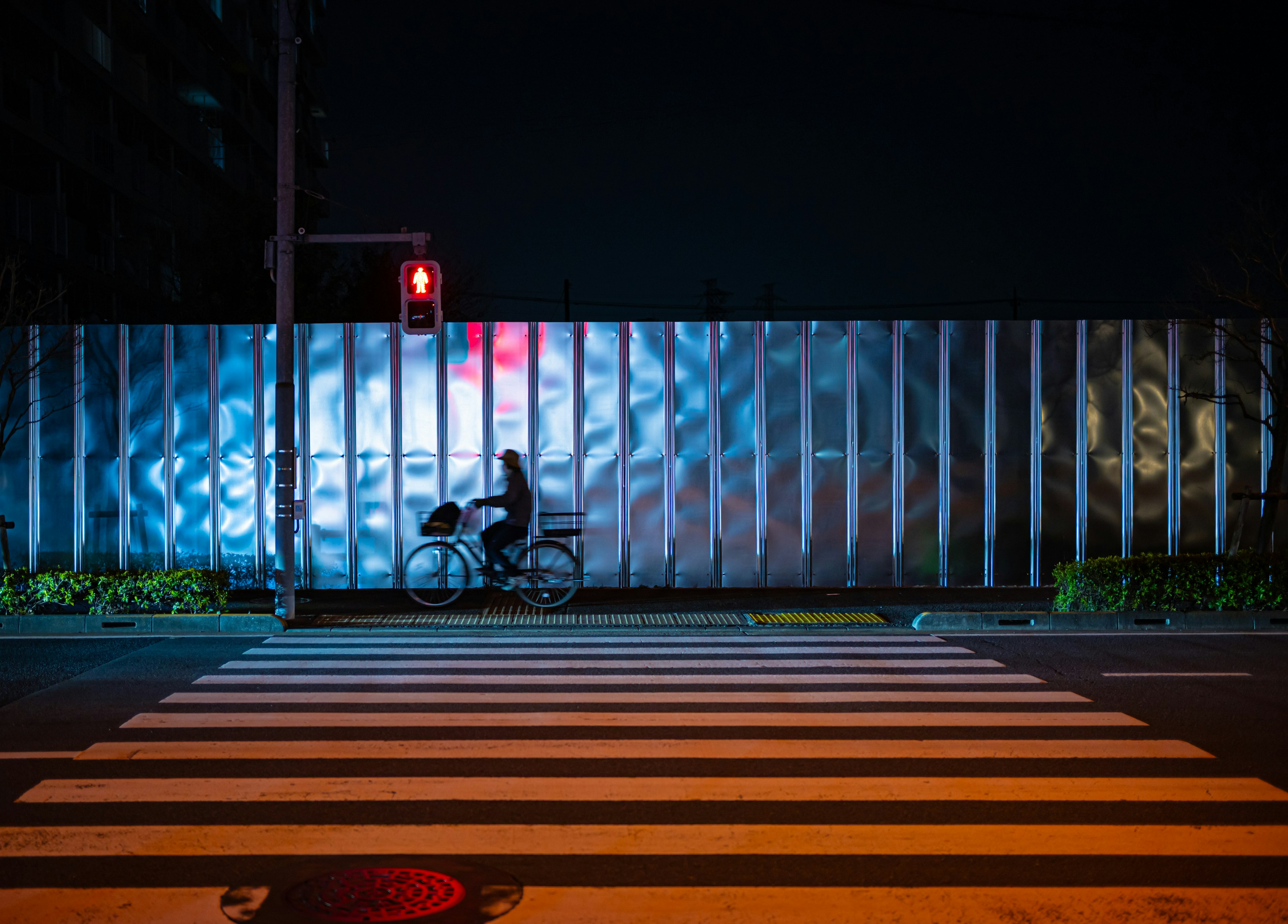 Une personne à vélo sur un passage piéton avec un feu rouge la nuit