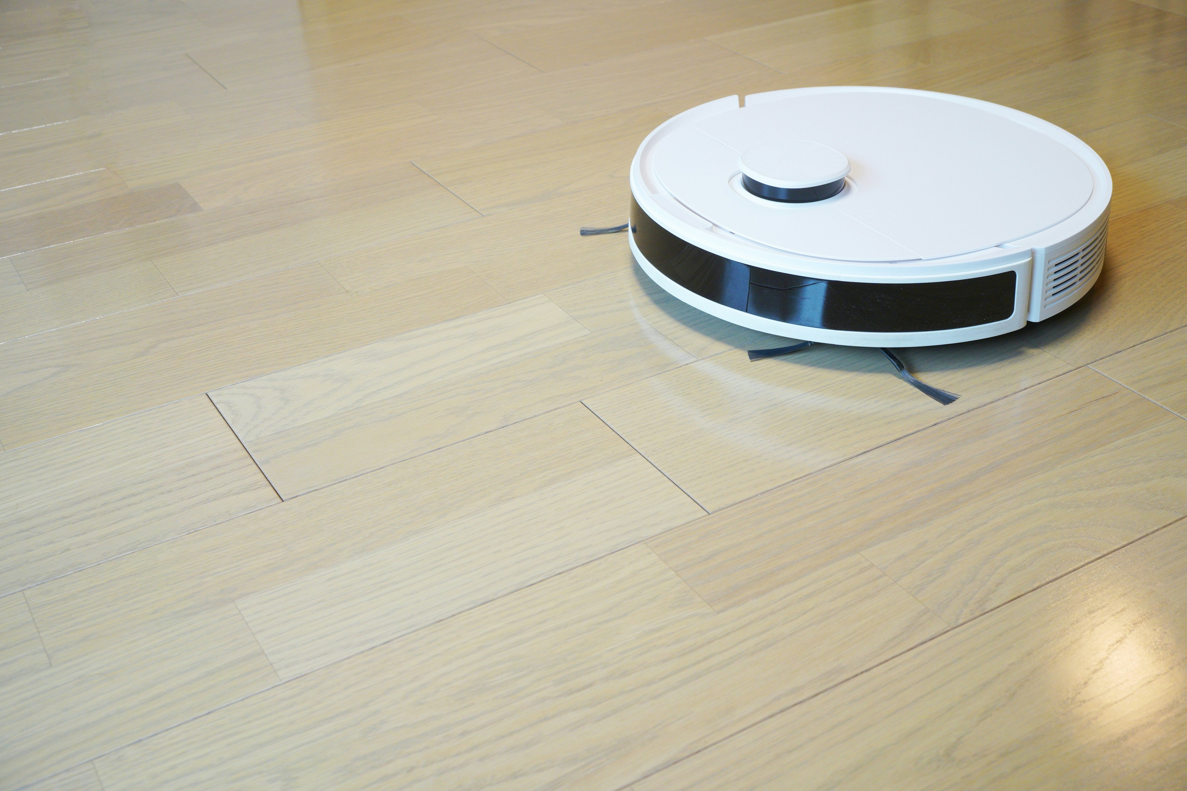 A white robotic vacuum cleaner moving on a wooden floor