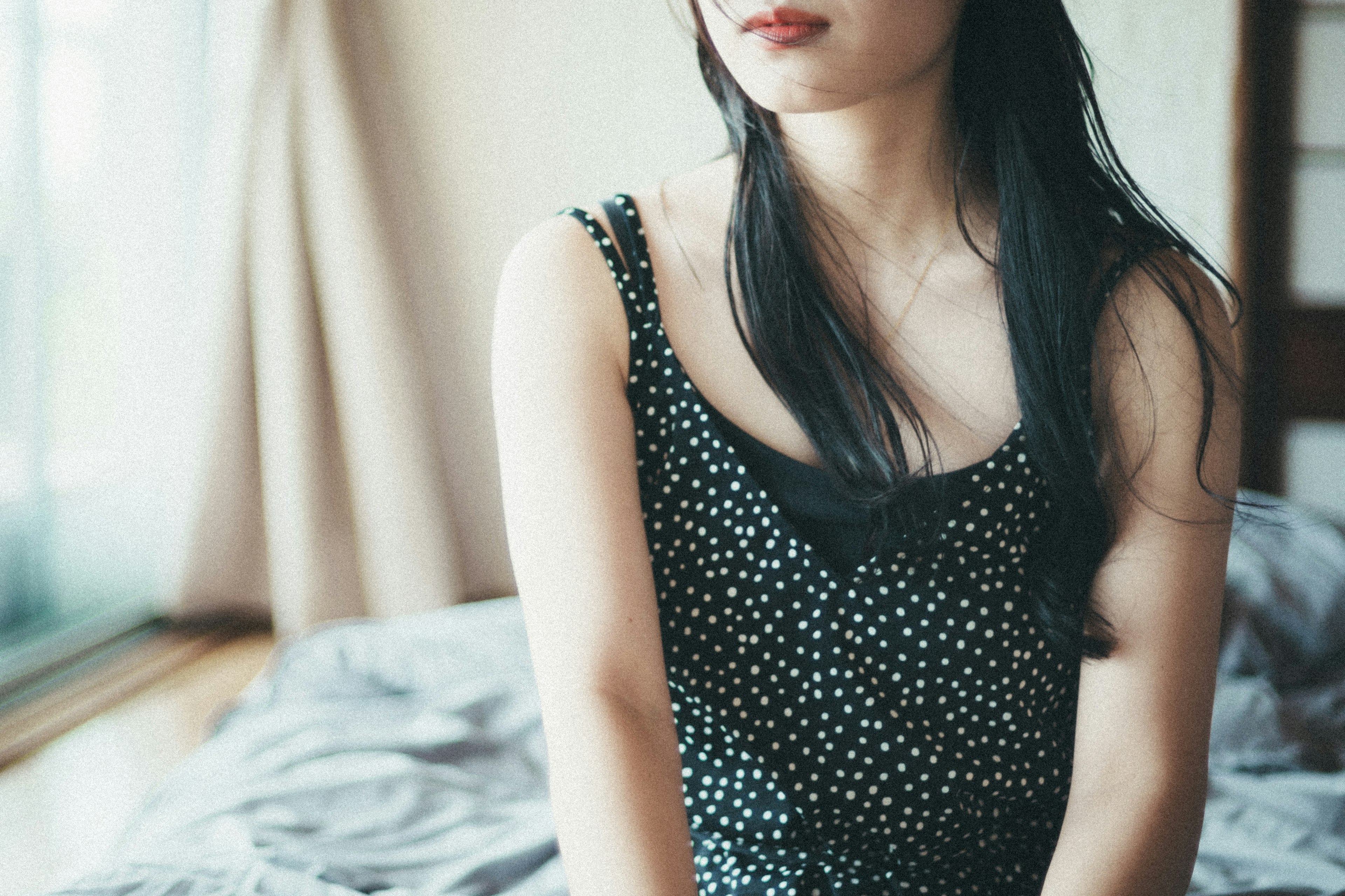 Upper body of a woman sitting near a window wearing a black polka dot dress