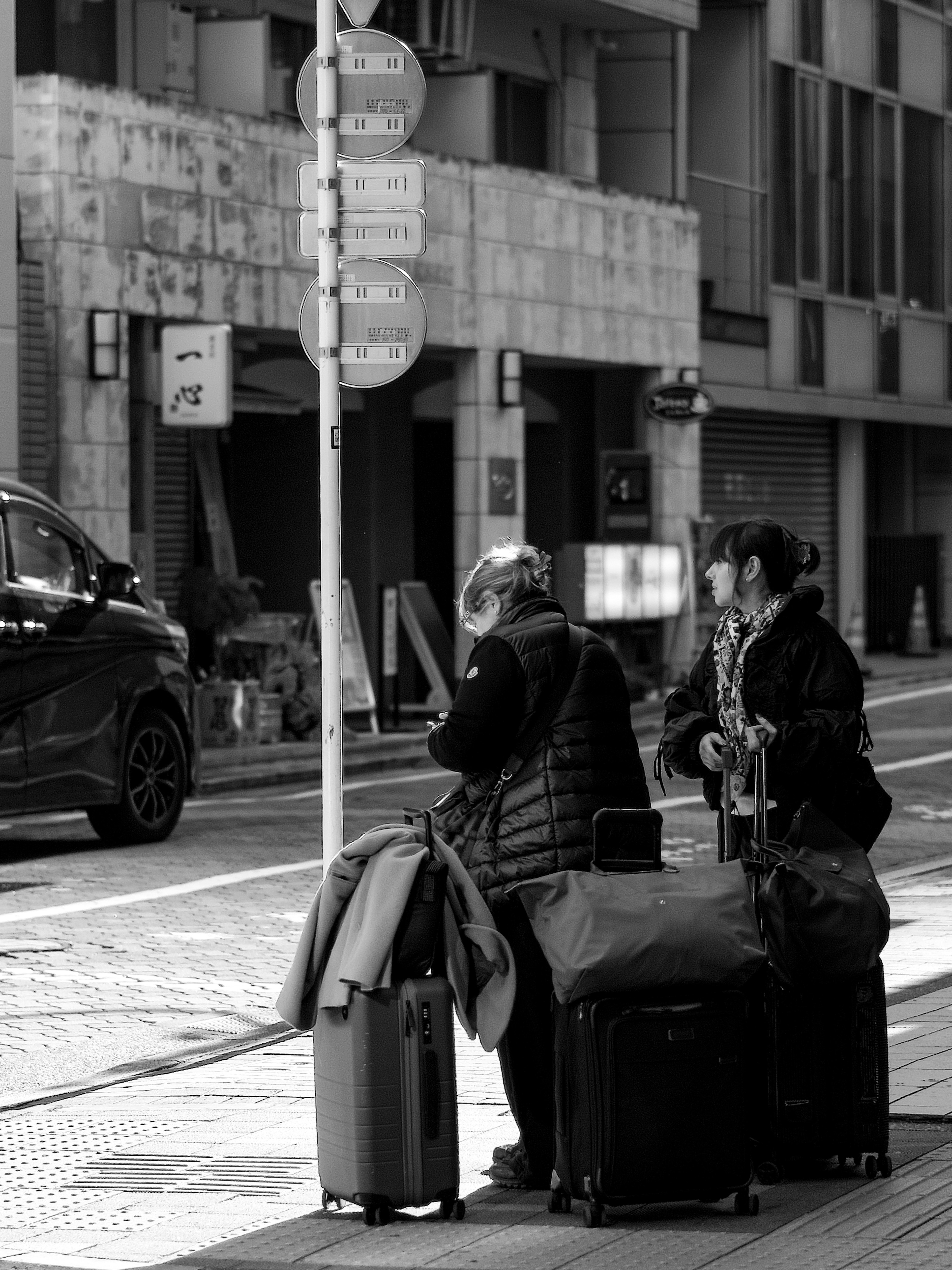 二人の旅行者がスーツケースを持って立っているモノクロの街角