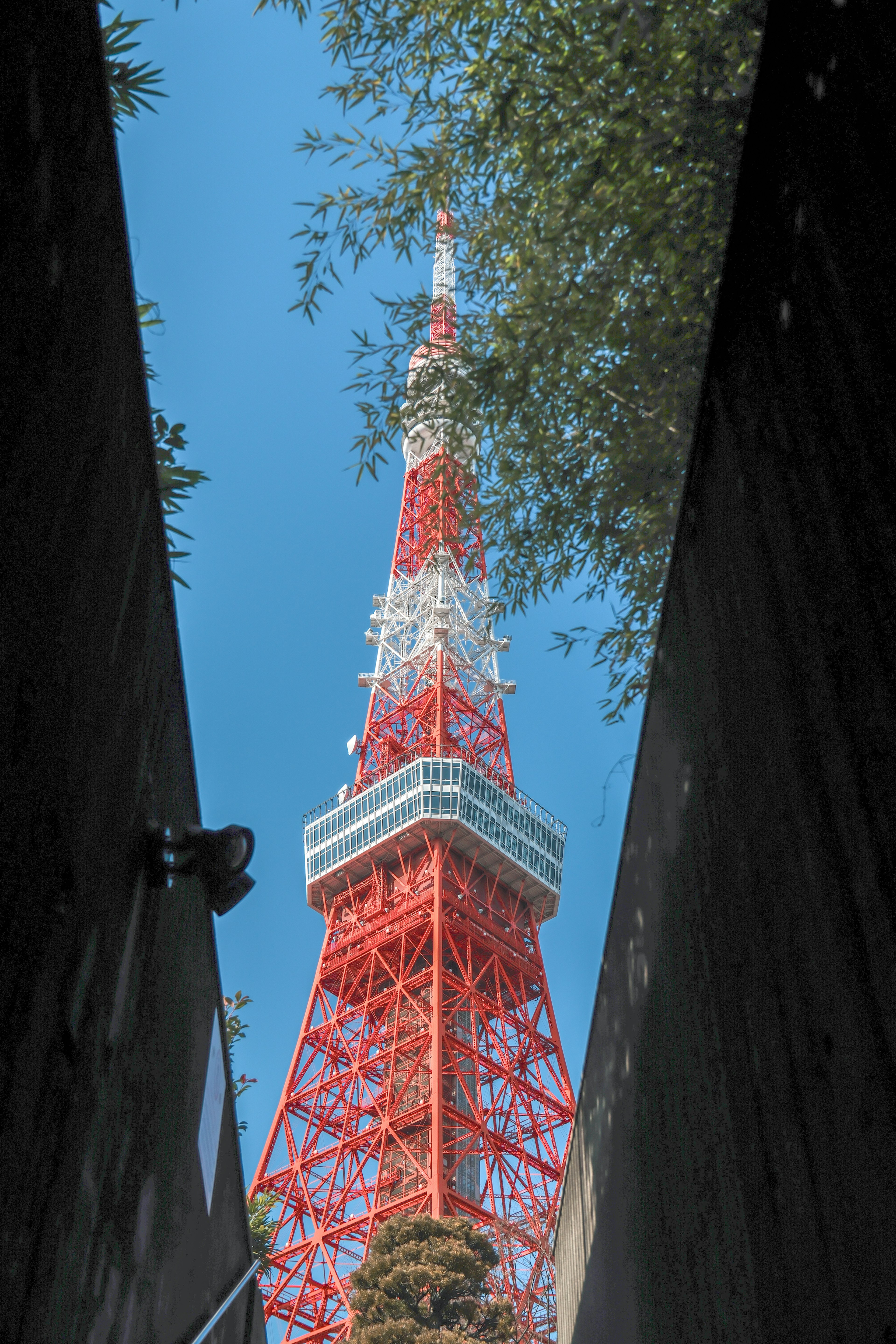 Pemandangan Menara Tokyo yang dibingkai oleh lorong sempit di bawah langit biru