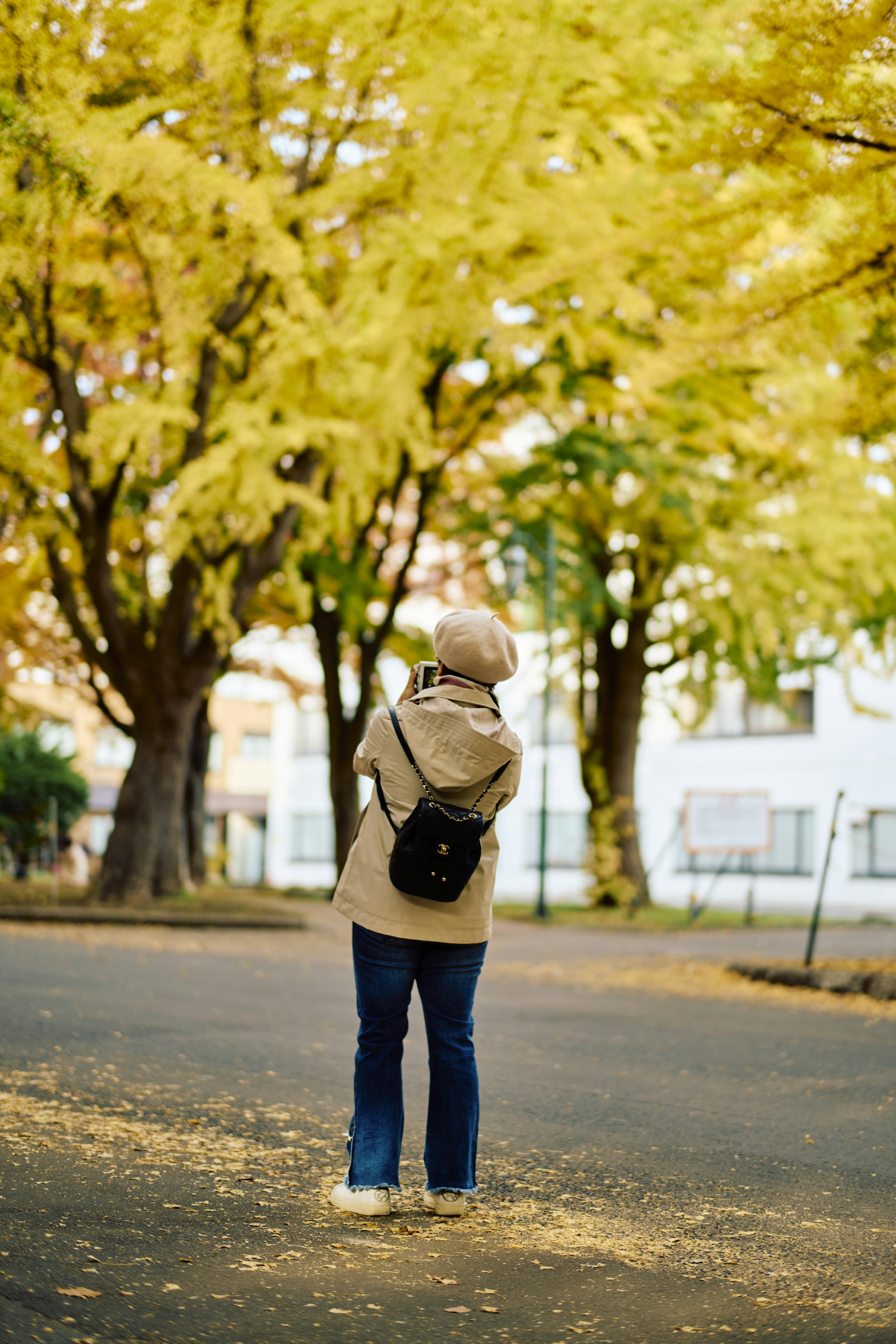 Femme en manteau beige se tenant sur un chemin entouré d'arbres jaunes d'automne