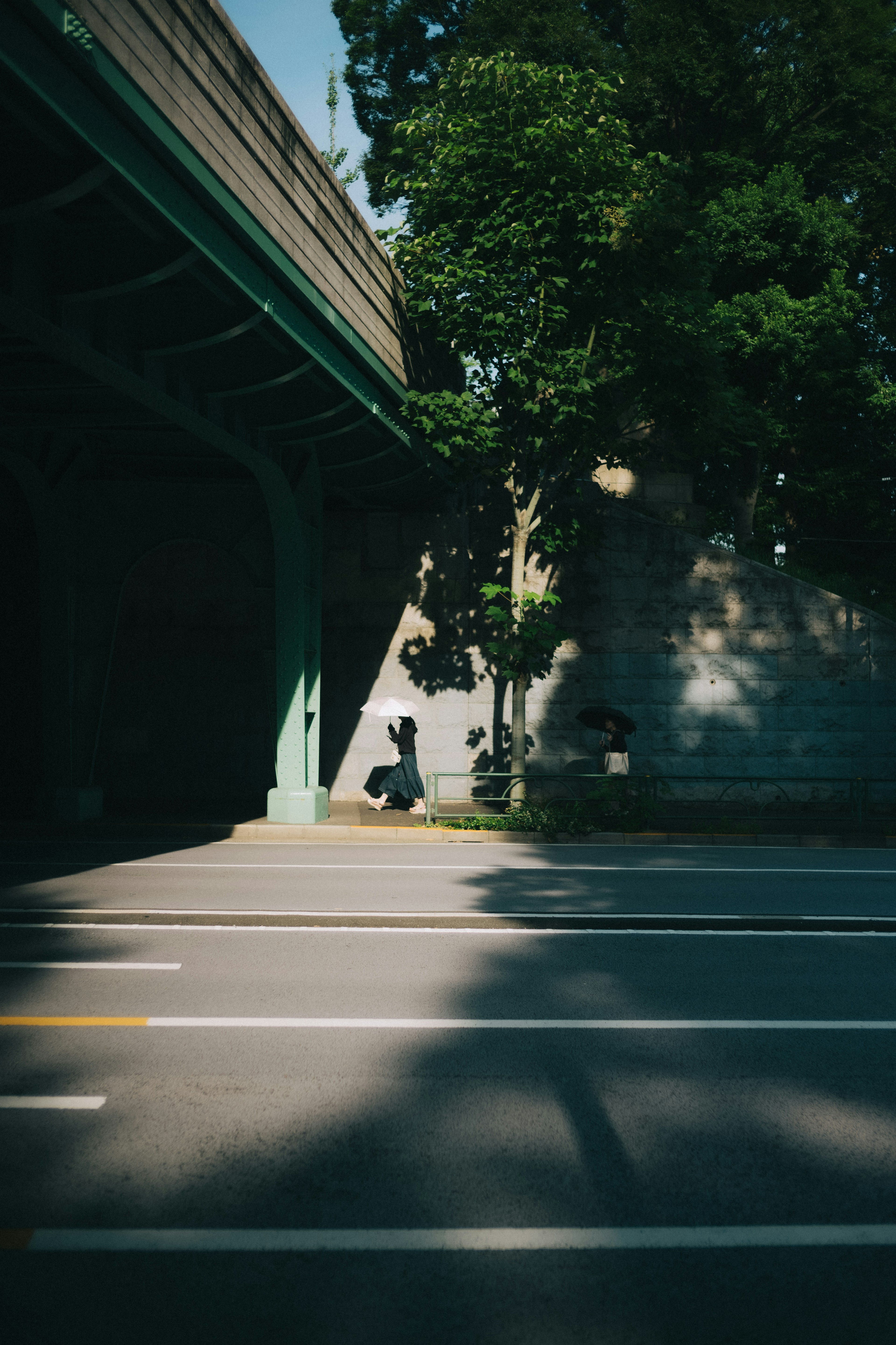 Escena de calle bajo un puente verde con sombras y árboles