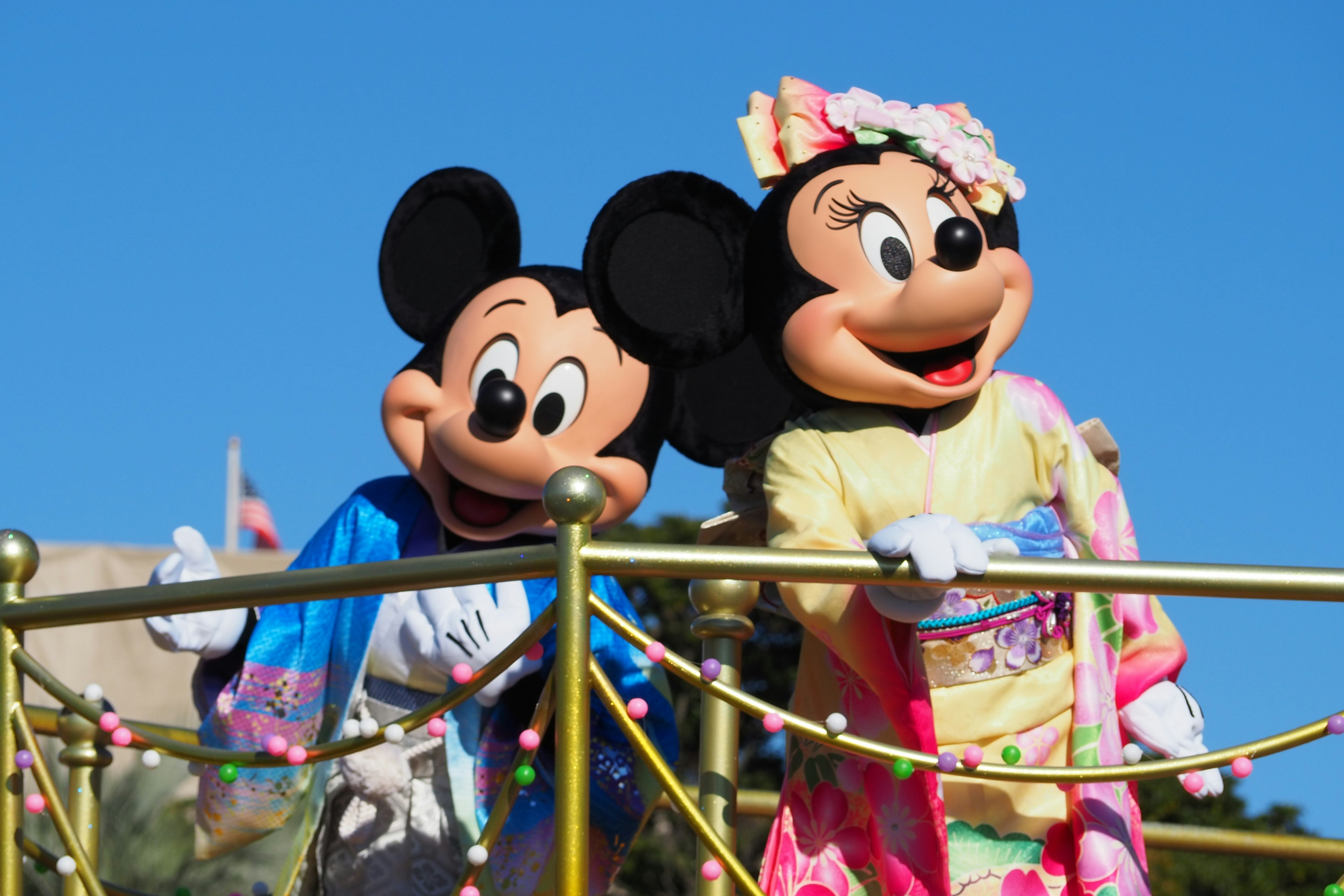 Mickey Mouse dan Minnie Mouse mengenakan kostum berwarna-warni tersenyum dan berpose