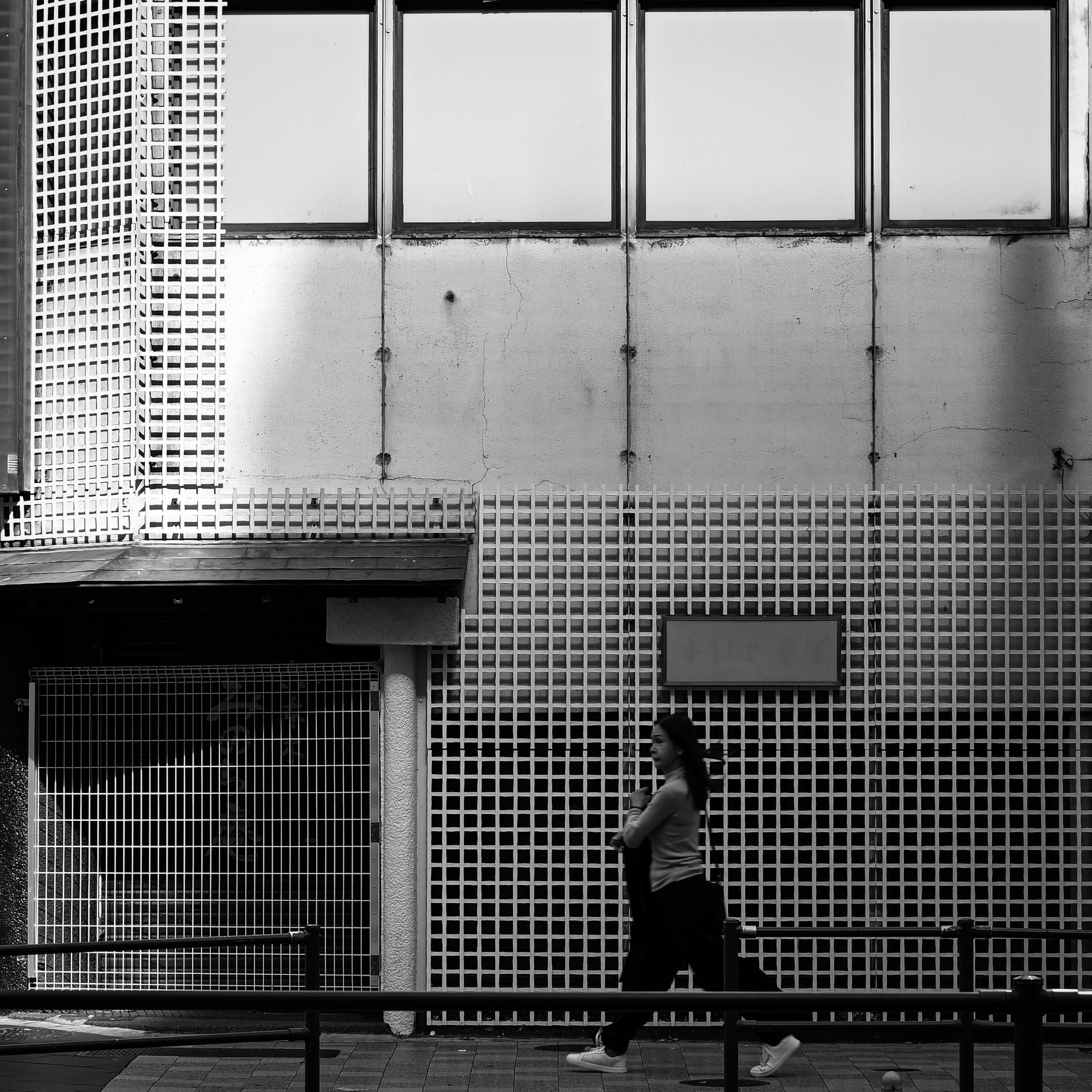 Una donna che corre in una strada della città con un muro a motivo a griglia