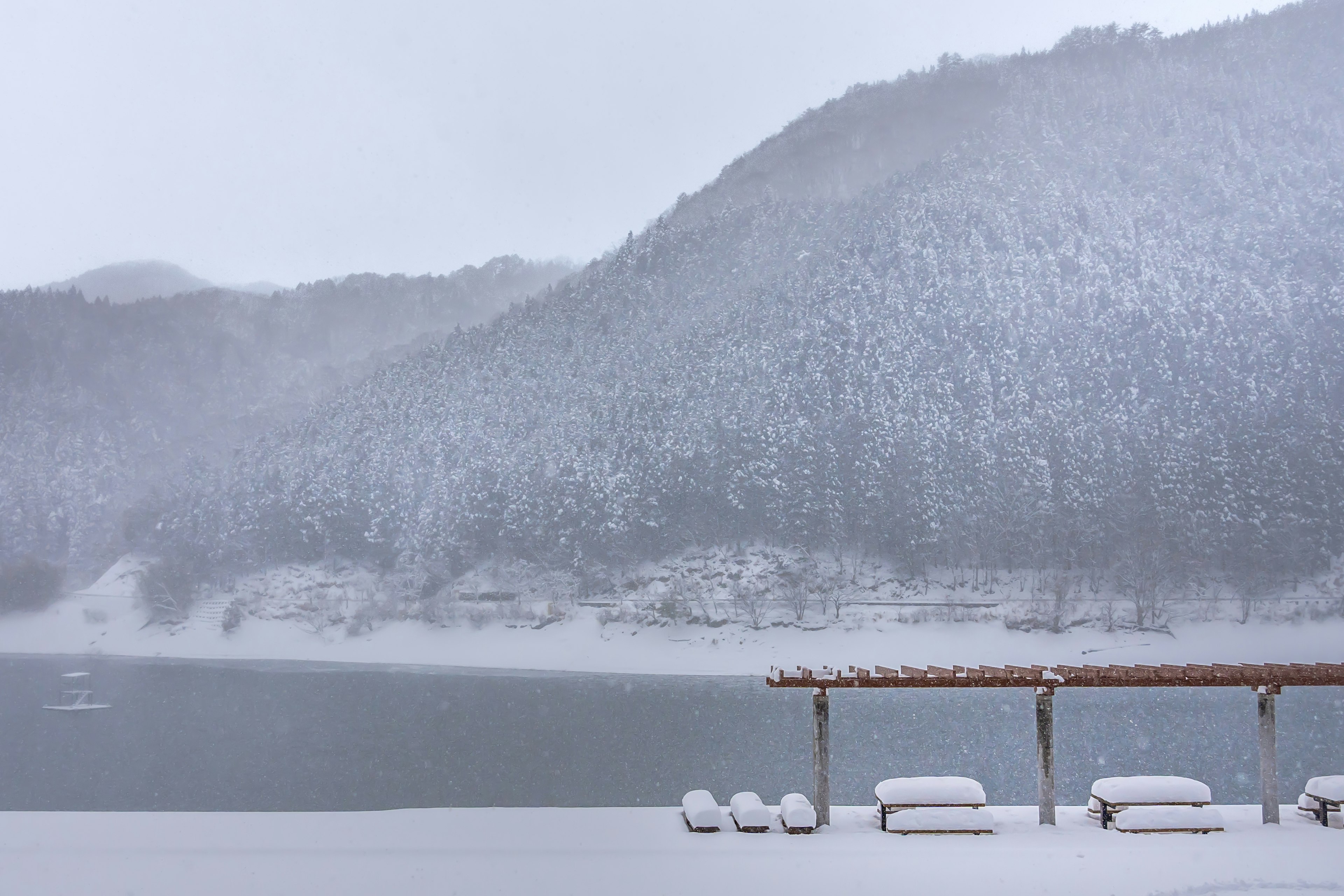 Snow-covered mountains and lake with a wooden structure and snow-covered benches