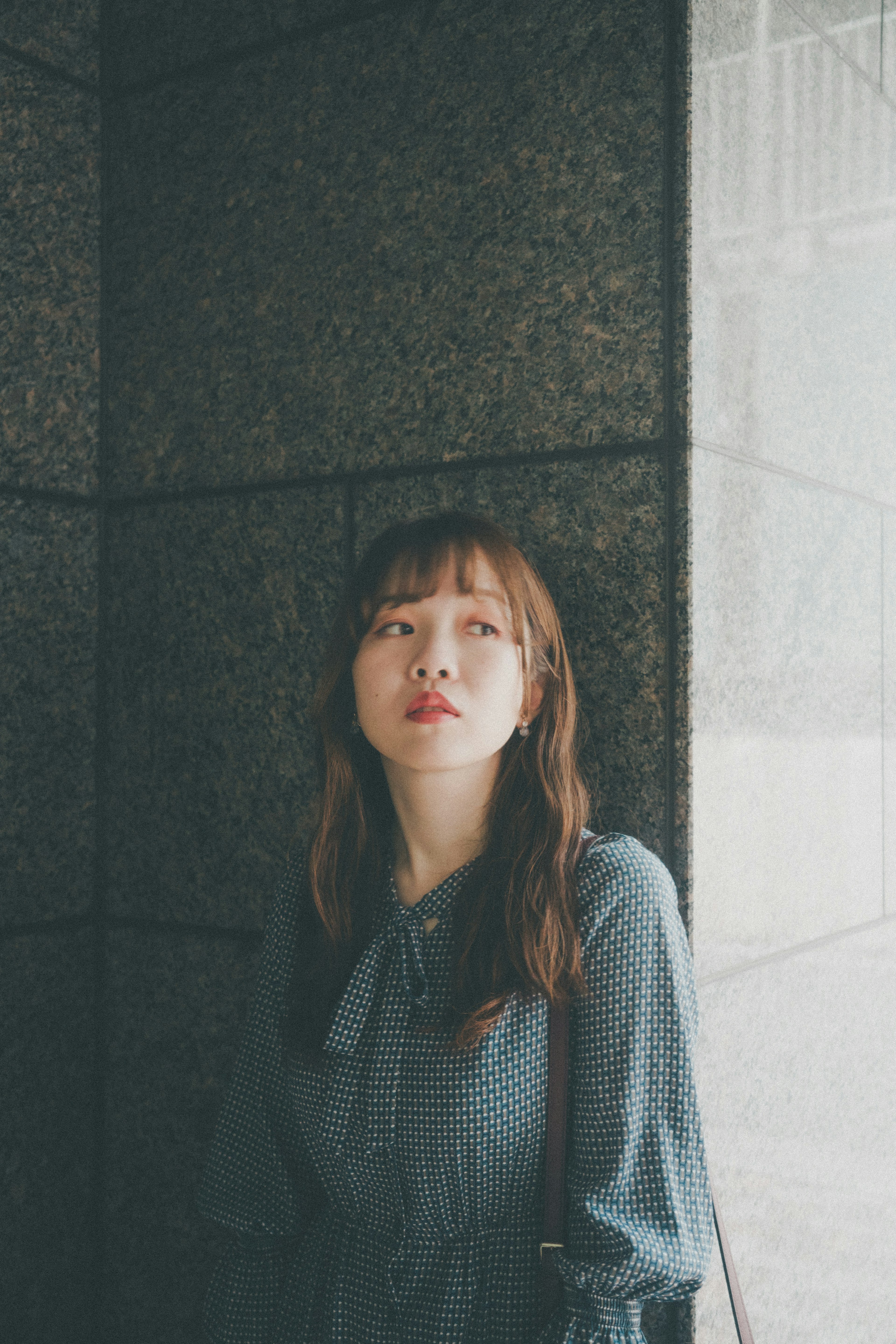 Portrait of a woman standing by a wall soft natural light illuminating her face